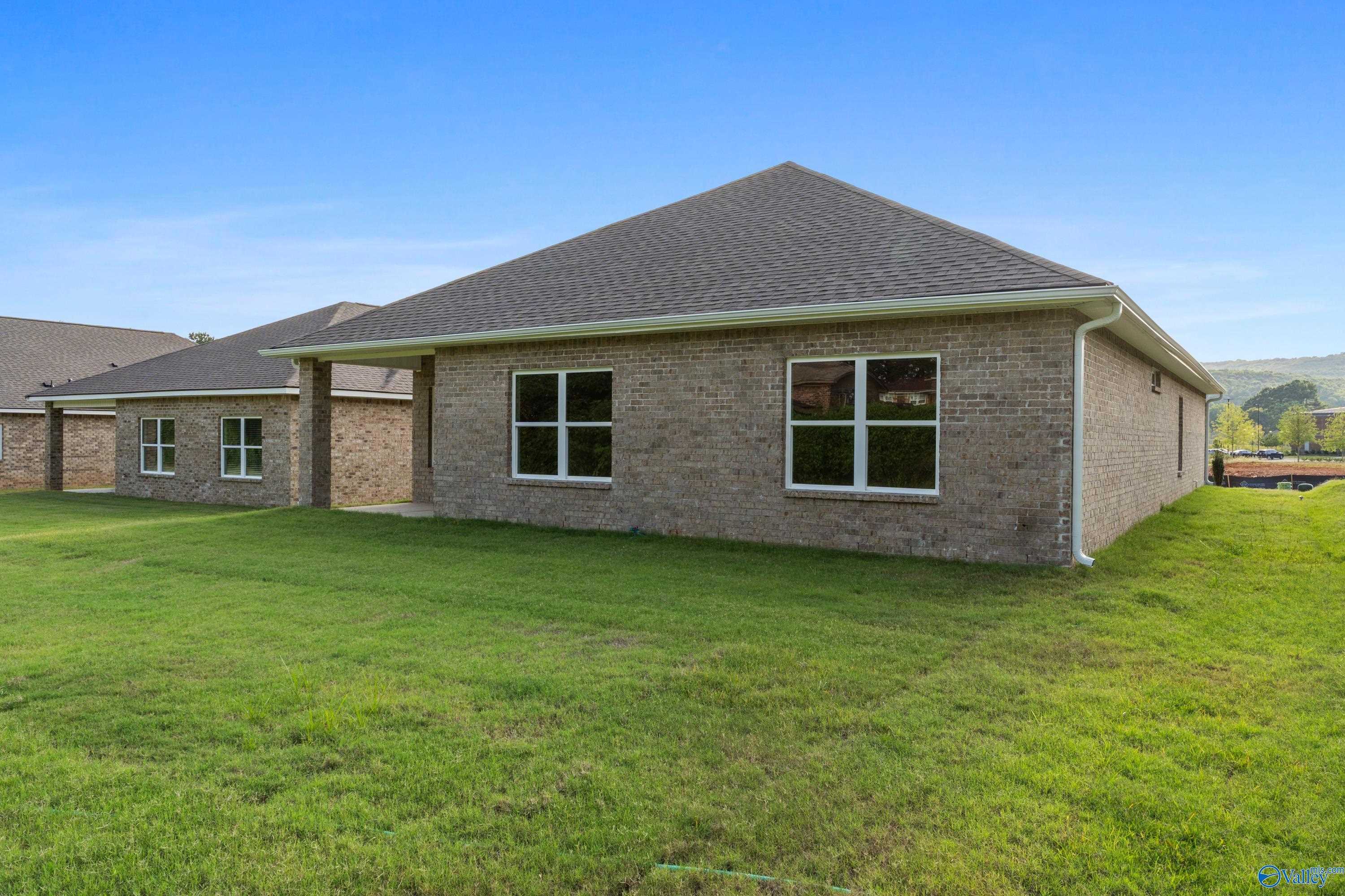 Brick 1-story home exterior with gabled roof, large windows, 2-car garage, lush green lawn in Jaguar Hills, Huntsville, Alabama