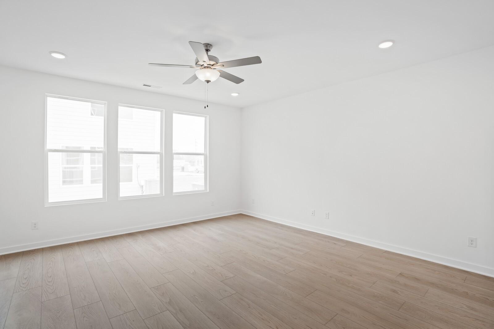 Bright, spacious bedroom with light wood flooring and ceiling fan in The Logan B floor plan at Calista Farms, Tennessee.
