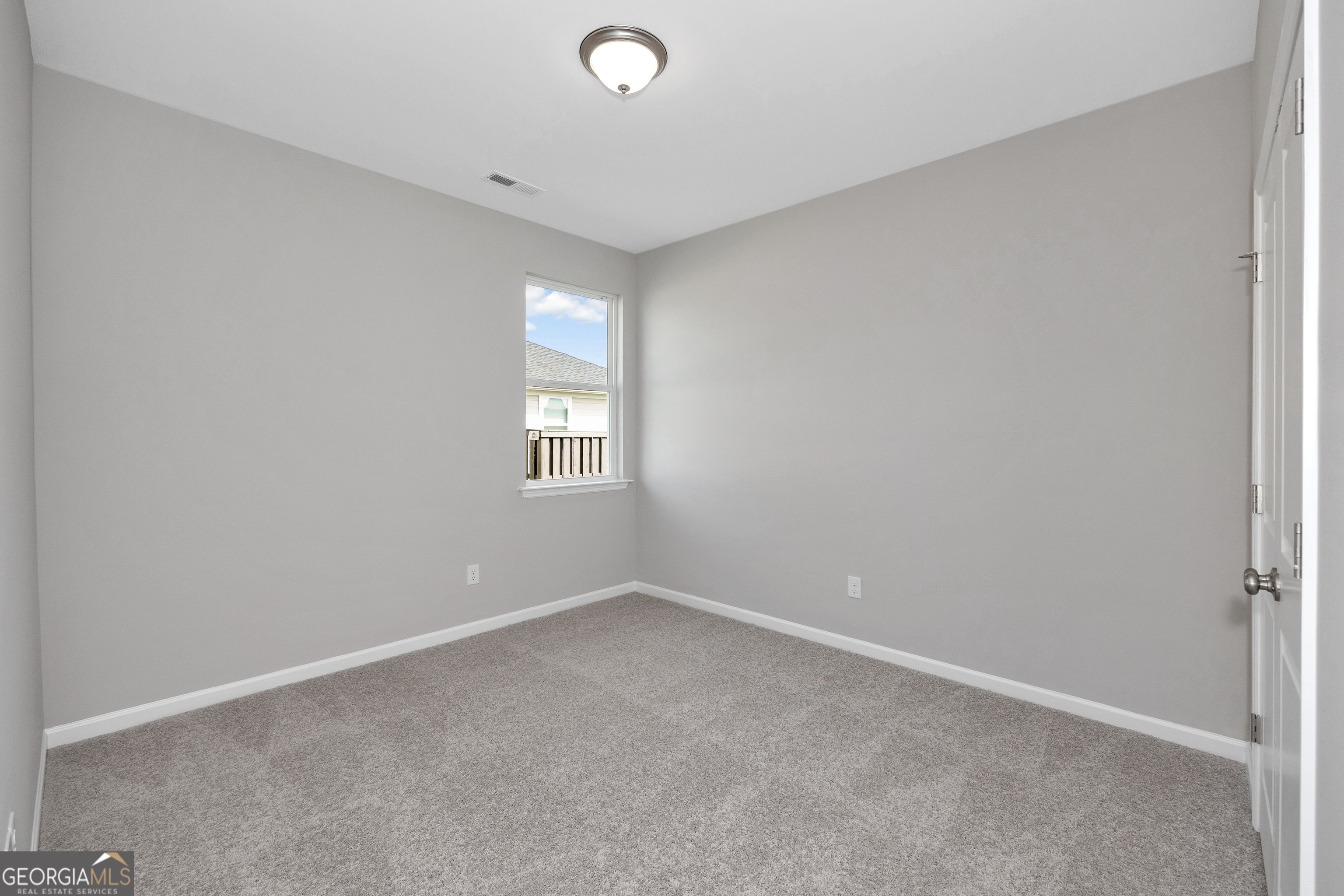 Bright secondary bedroom with light gray walls, carpeted floor, and window view in Evermore Homes The Luna, Perry, GA