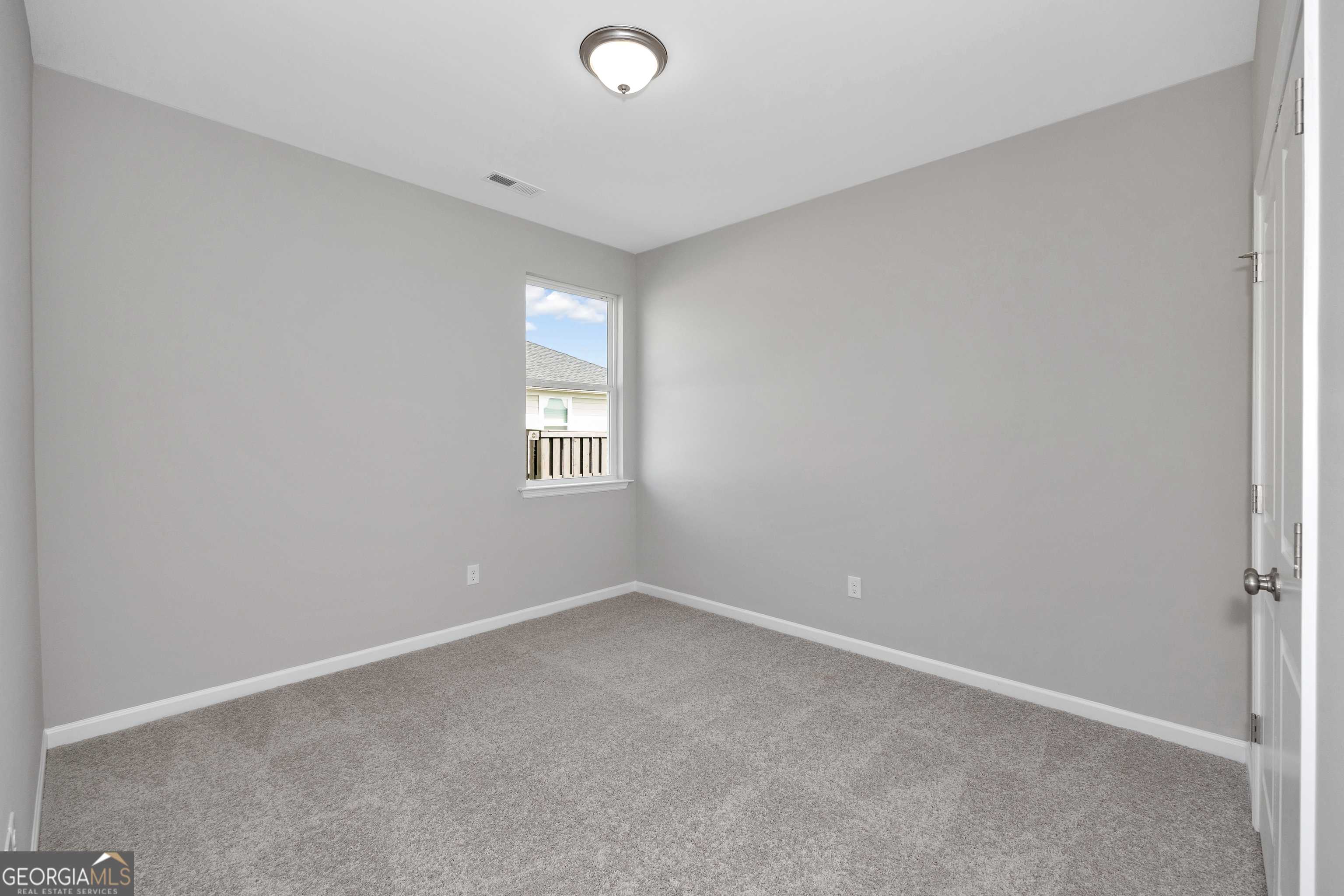Bright secondary bedroom with light gray walls, carpeted floor, and window view in Evermore Homes The Luna, Perry, GA