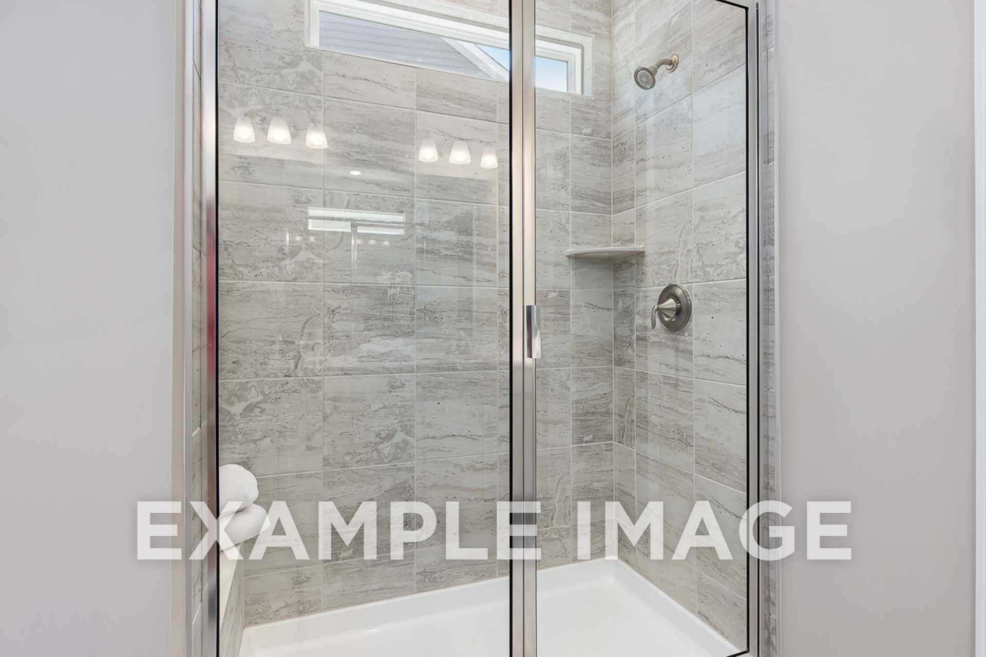 Modern walk-in shower in The Ash E master bath with frameless glass doors, gray tile walls, and built-in niche