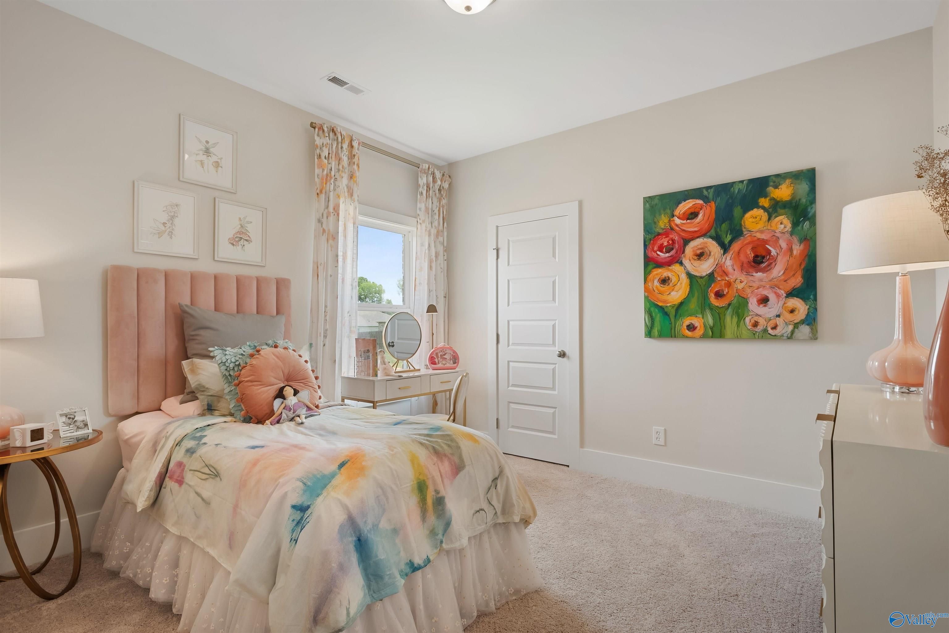 Cozy girl's bedroom with pink headboard, colorful floral bedding, vanity mirror, and abstract flower art in Davidson Homes The Everett, New Market, Alabama
