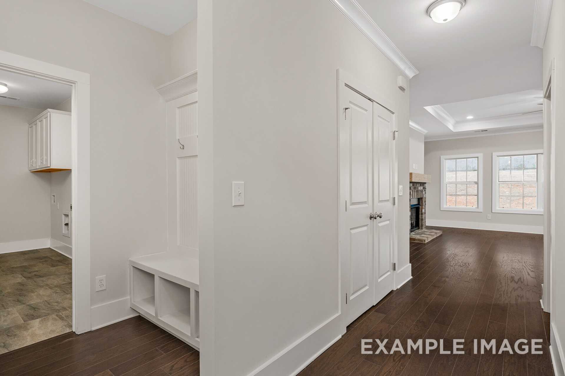 The Rockford mudroom and laundry area featuring built-in bench, coat closet, hardwood floors, and open hallway to living space