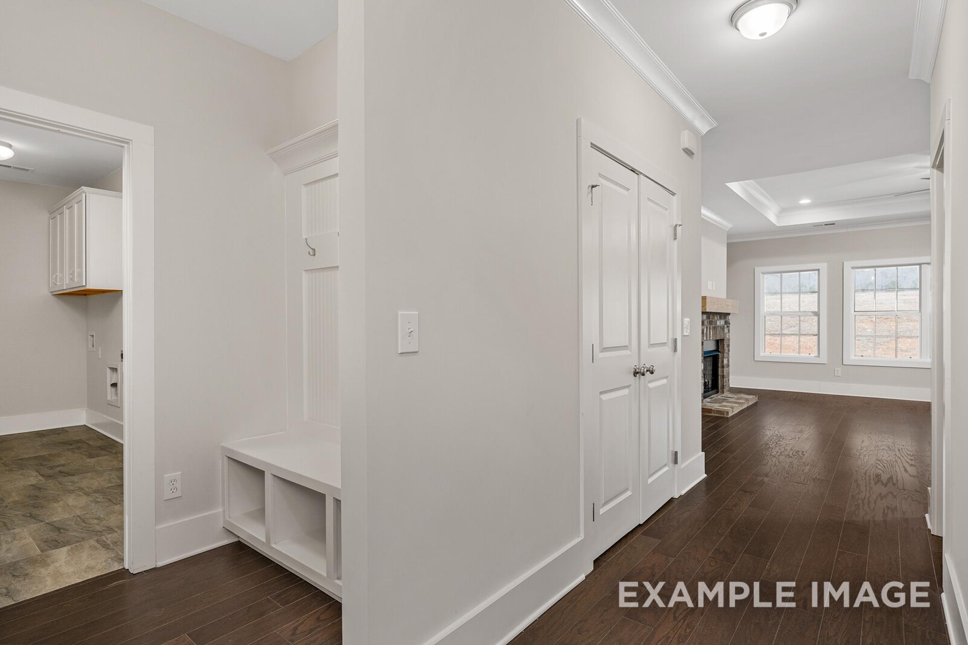 Spacious mudroom and laundry in The Rockford by Davidson Homes, with built-in bench, coat closet, hardwood floors, and beige walls