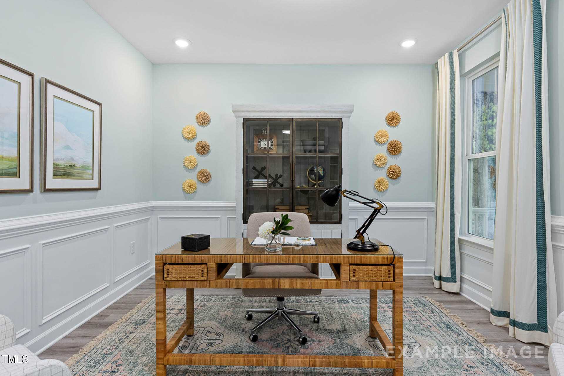 Cozy home office with wooden desk, rattan chair, glass-door bookshelves, and large window in Davidson Homes The Magnolia B, Lillington NC