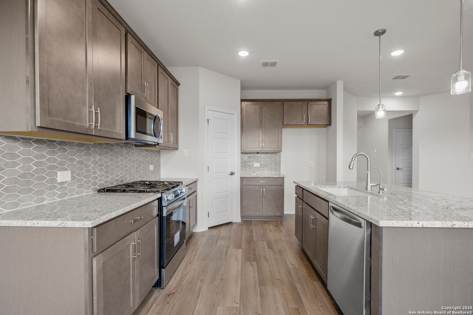 Modern gray kitchen with quartz counters, stainless appliances, geometric tile backsplash in The Asheville J, San Antonio home