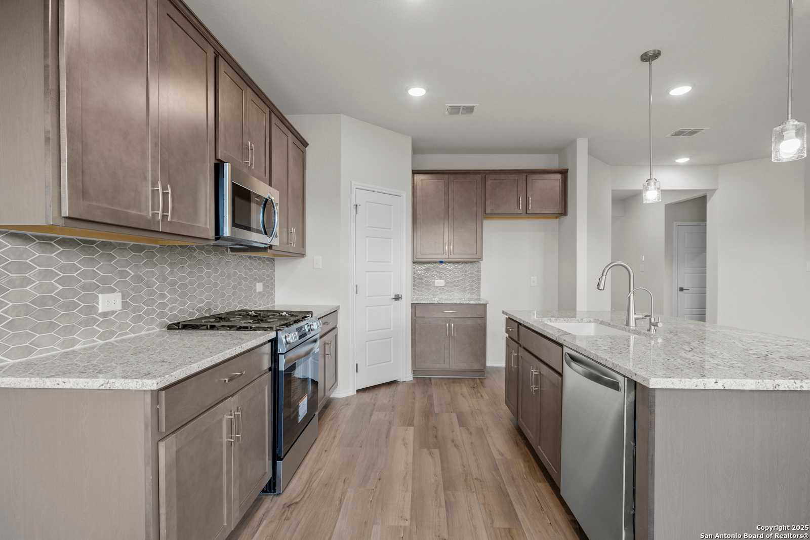Modern gray kitchen with quartz counters, stainless appliances, geometric tile backsplash in The Asheville J, San Antonio home