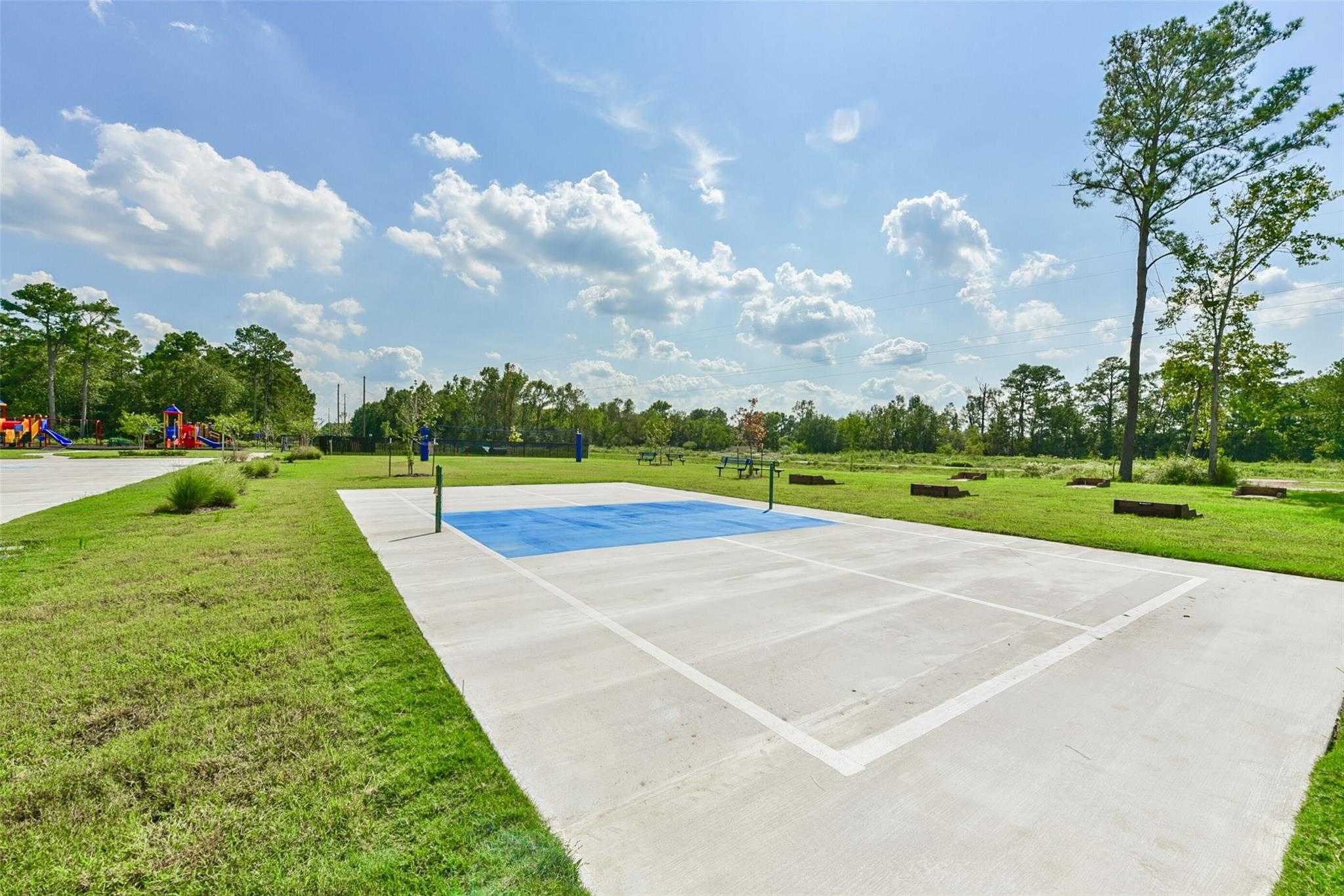 Community sports court with blue pickleball surface, basketball hoop, playground, and pine trees in The Villages at WestPointe, Dayton, Texas