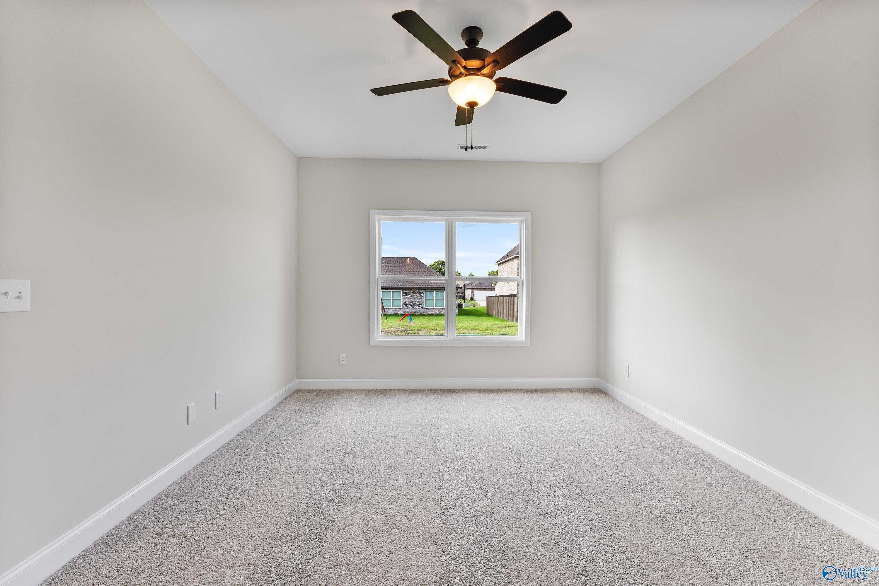 Bright empty bedroom with ceiling fan, beige carpet, and window view of green yard in Davidson Homes The Franklin B, Hazel Green, Alabama