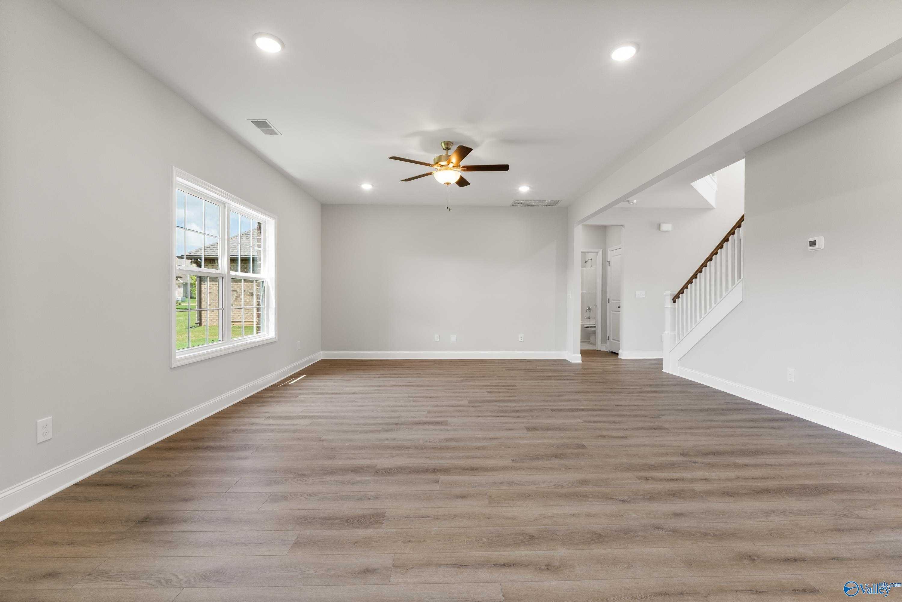 Bright living room with hardwood floors, ceiling fan, large windows, and open staircase in Davidson Homes The Madison A, Toney, Alabama