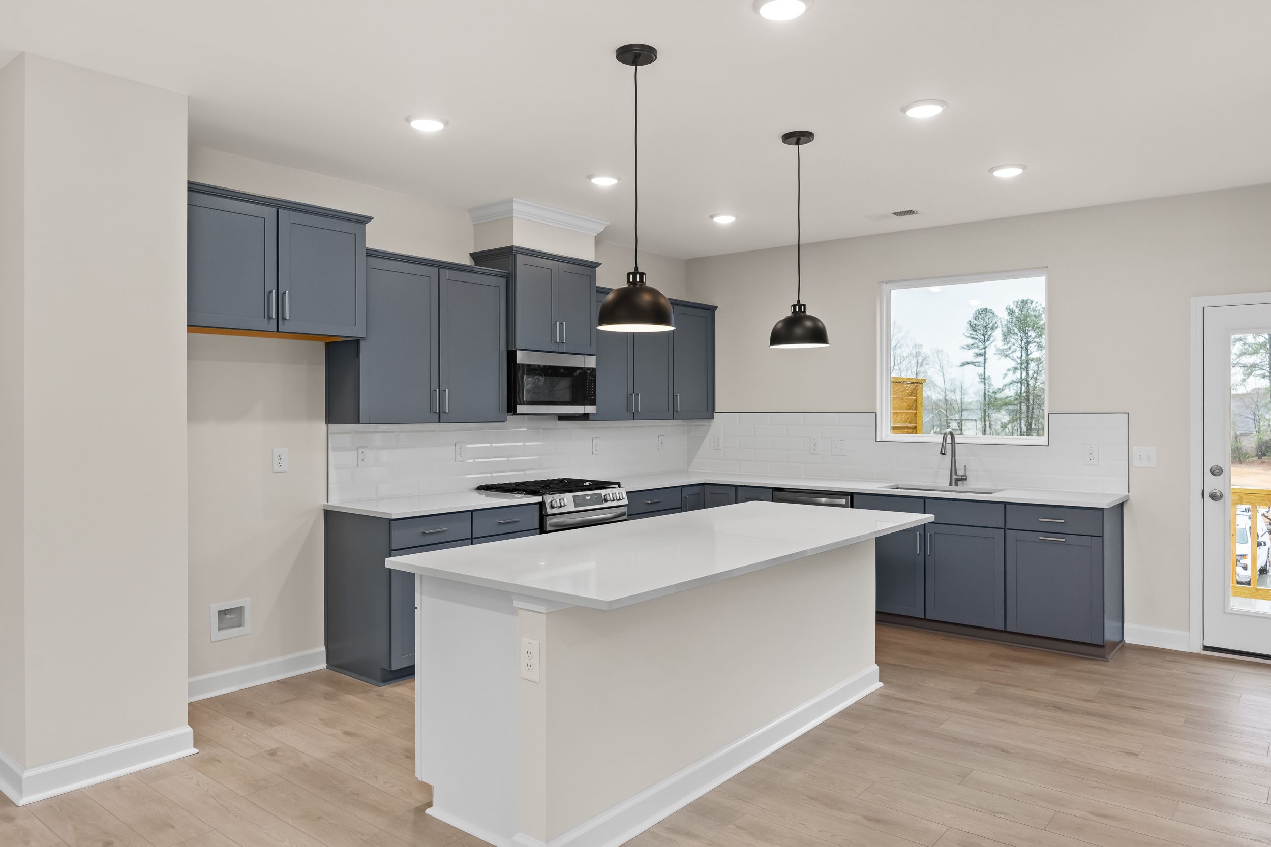 Spacious navy cabinet kitchen in Forestville Yard Townhomes, Knightdale NC with white quartz island, stainless appliances, and hardwood floors