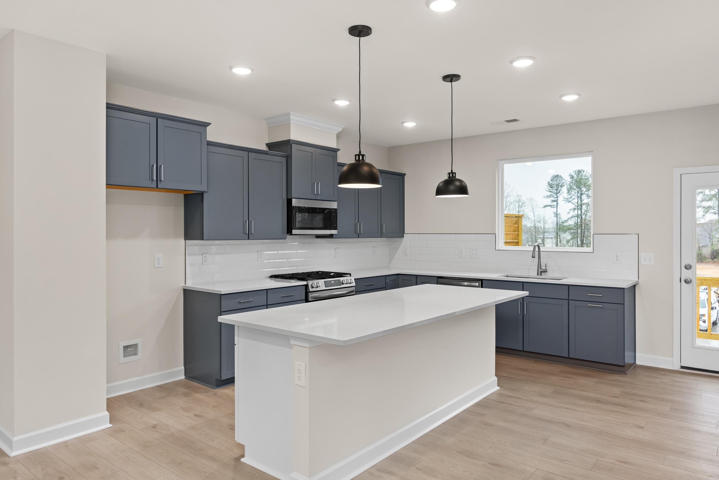 Spacious navy cabinet kitchen in Forestville Yard Townhomes, Knightdale NC with white quartz island, stainless appliances, and hardwood floors