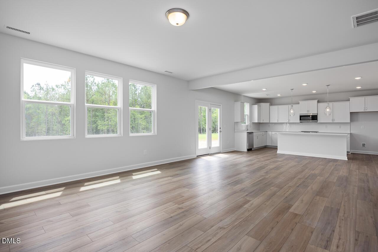Bright open living area with hardwood floors, large windows overlooking woods, and white kitchen island in The Hickory II B, Zebulon, NC