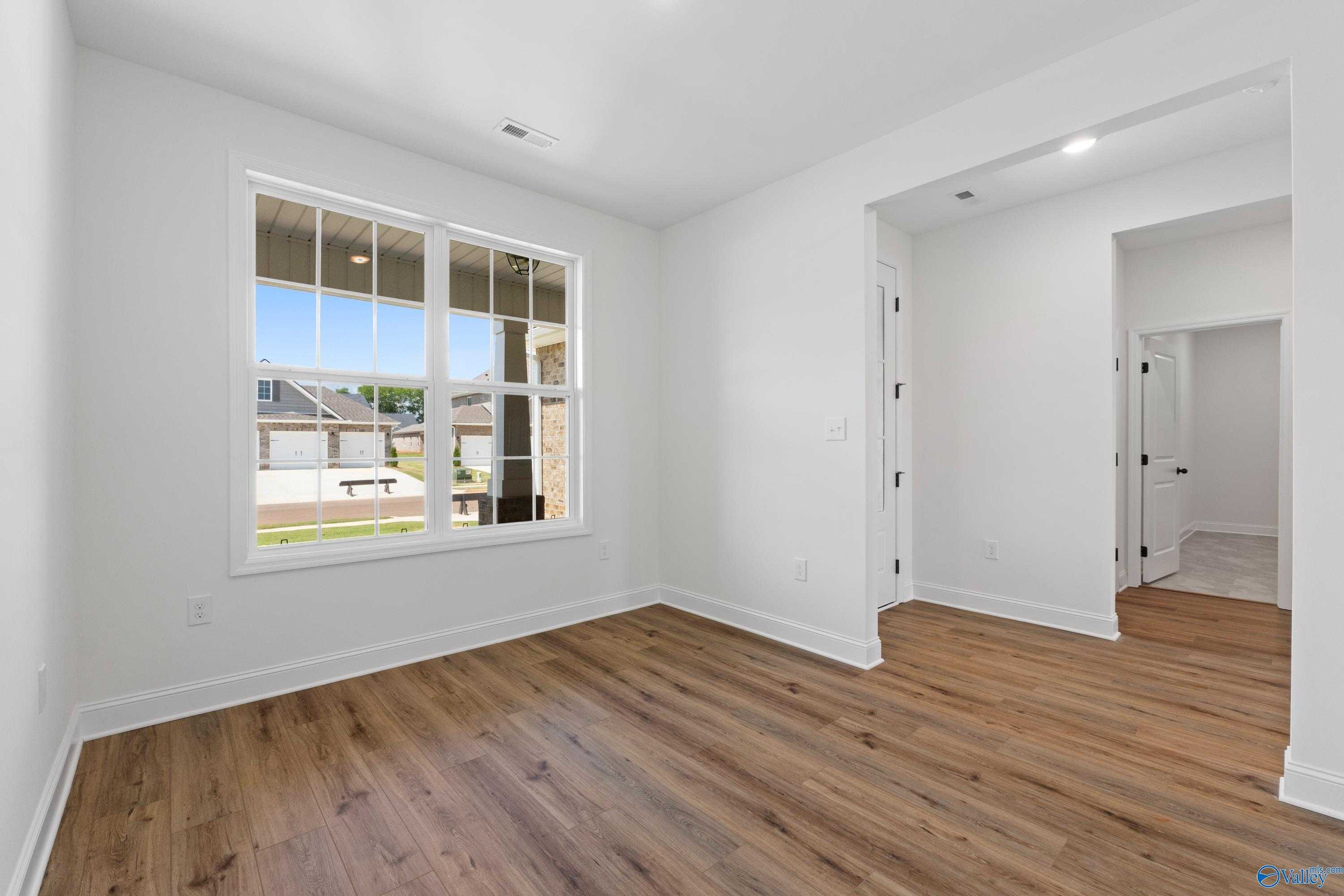 Bright living room with large window overlooking green yard and warm hardwood floors in Davidson Homes The Rockford B, Toney, Alabama