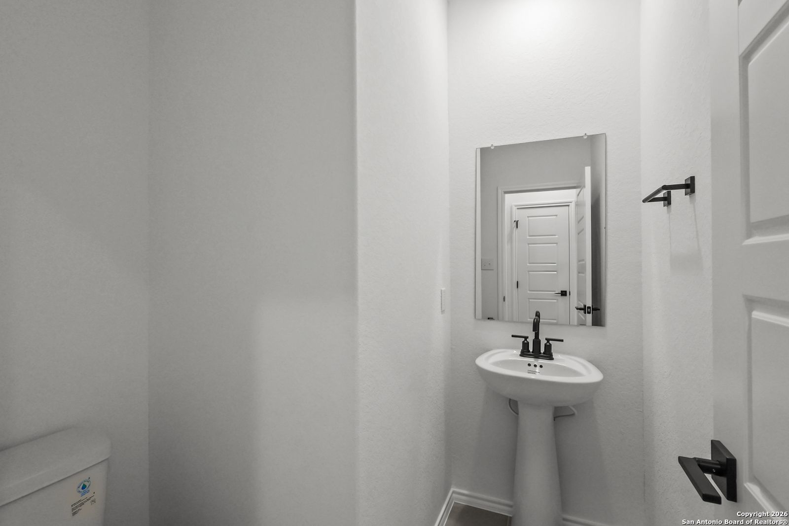 Elegant powder room with pedestal sink, mirror, and toilet in Davidson Homes The Douglas E, San Antonio, Texas