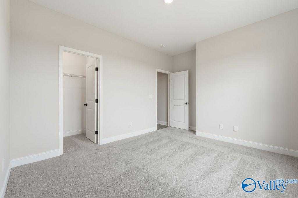 Spacious empty bedroom with beige walls, gray carpet, walk-in closet, and bathroom door in Davidson Homes The Rockford B, Hartselle, AL