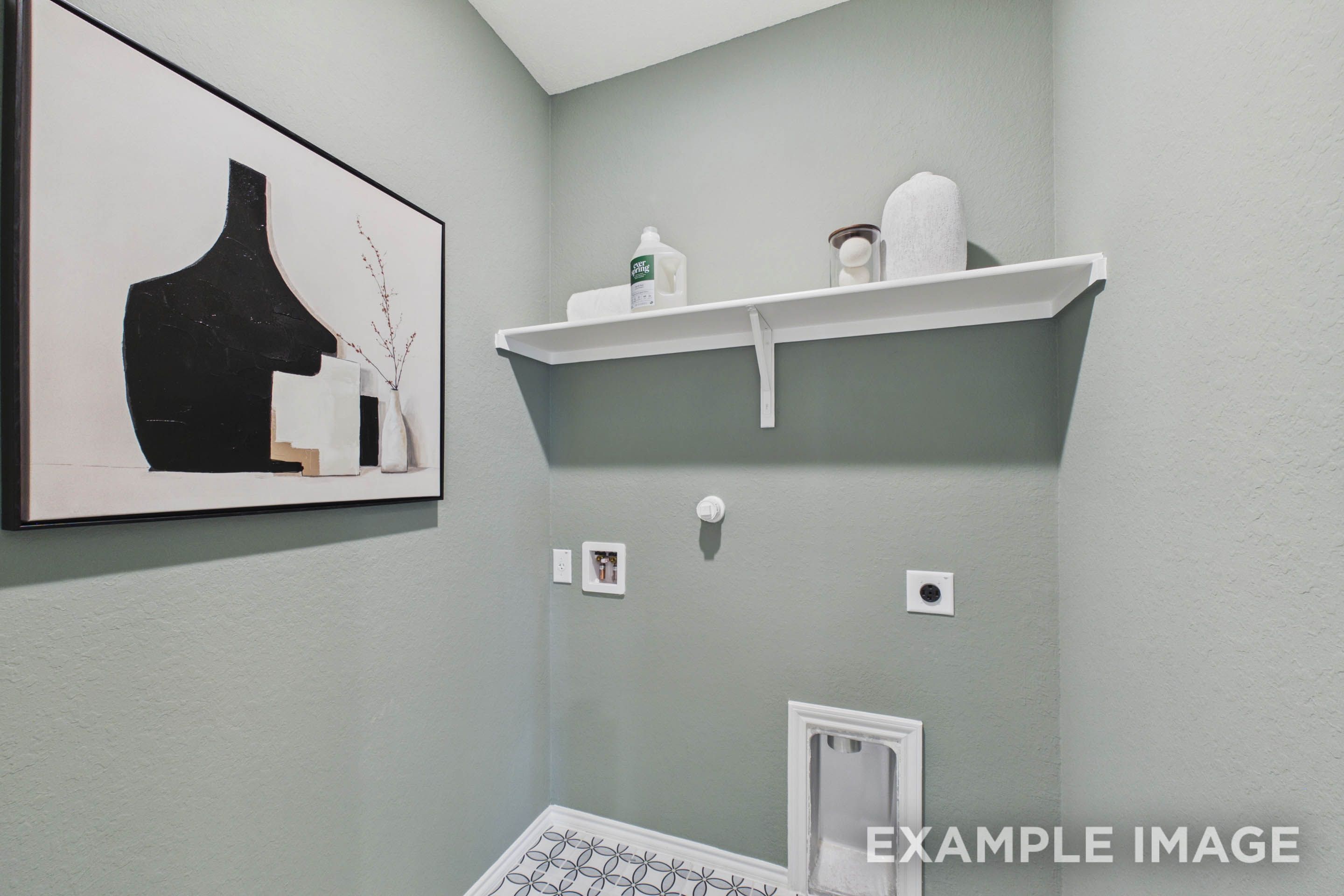 Functional laundry room in The Laurel G floor plan featuring sage green walls, wall-mounted shelving, and patterned tile.