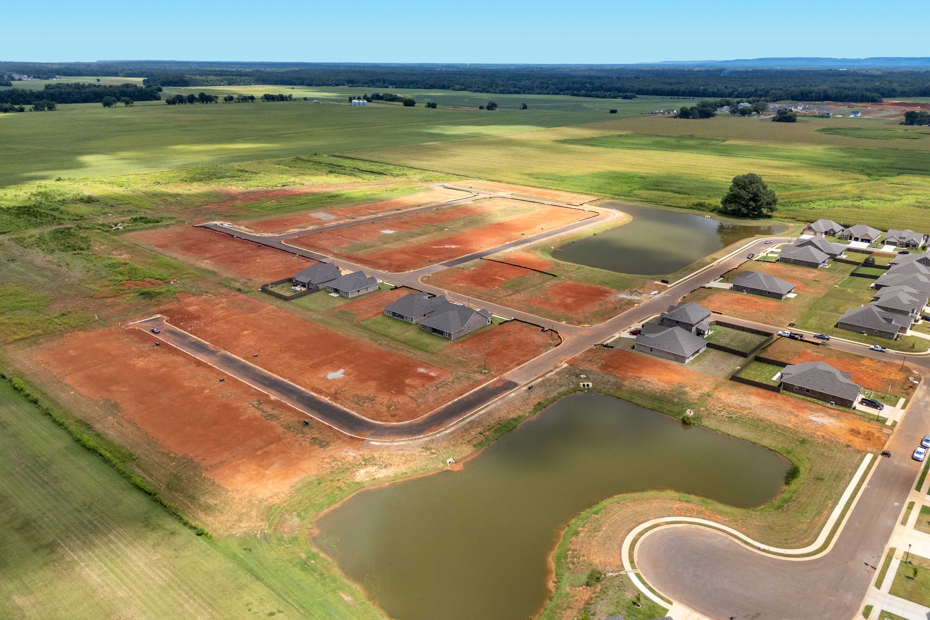 Aerial view of Kendall Downs in Toney Alabama with new homes, red dirt lots, ponds, and surrounding green fields by Davidson Homes