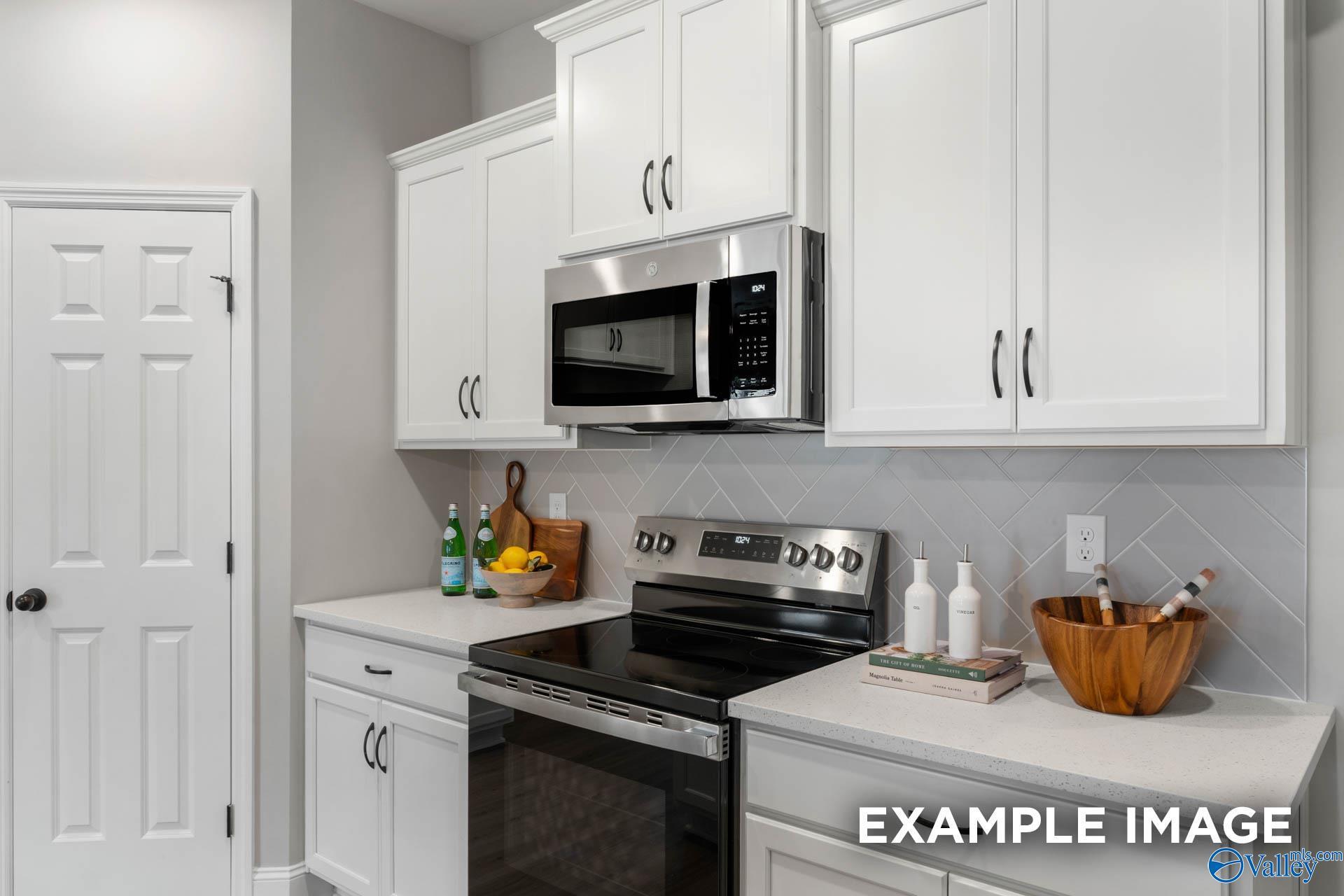 Modern kitchen with white cabinets, stainless steel appliances, and herringbone backsplash in The Daphne D, Huntsville.