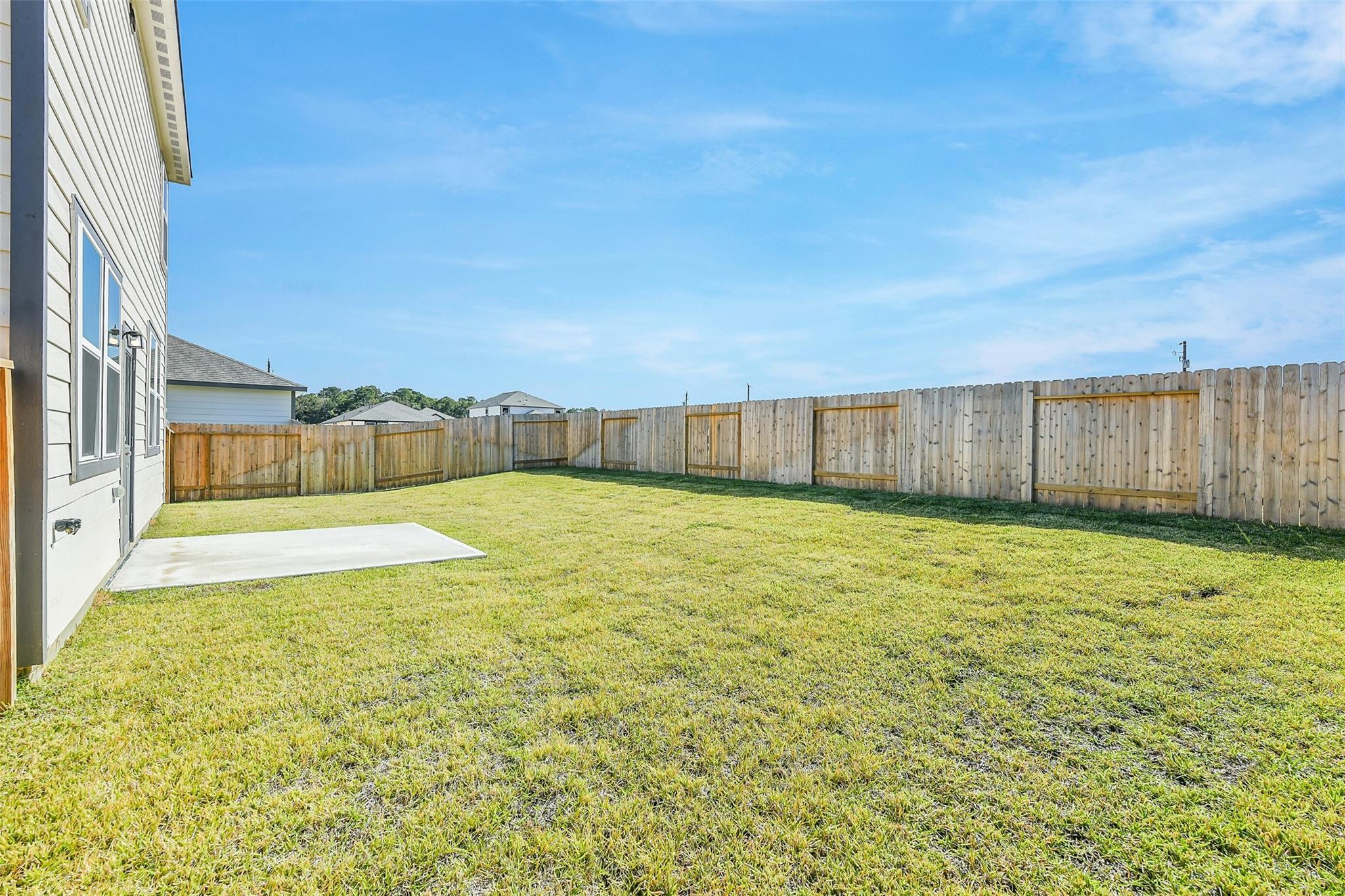 Private backyard with lush green lawn, concrete patio, and wooden privacy fence in Davidson Homes The San Marcos E, Liberty Estates, Cleveland, Texas