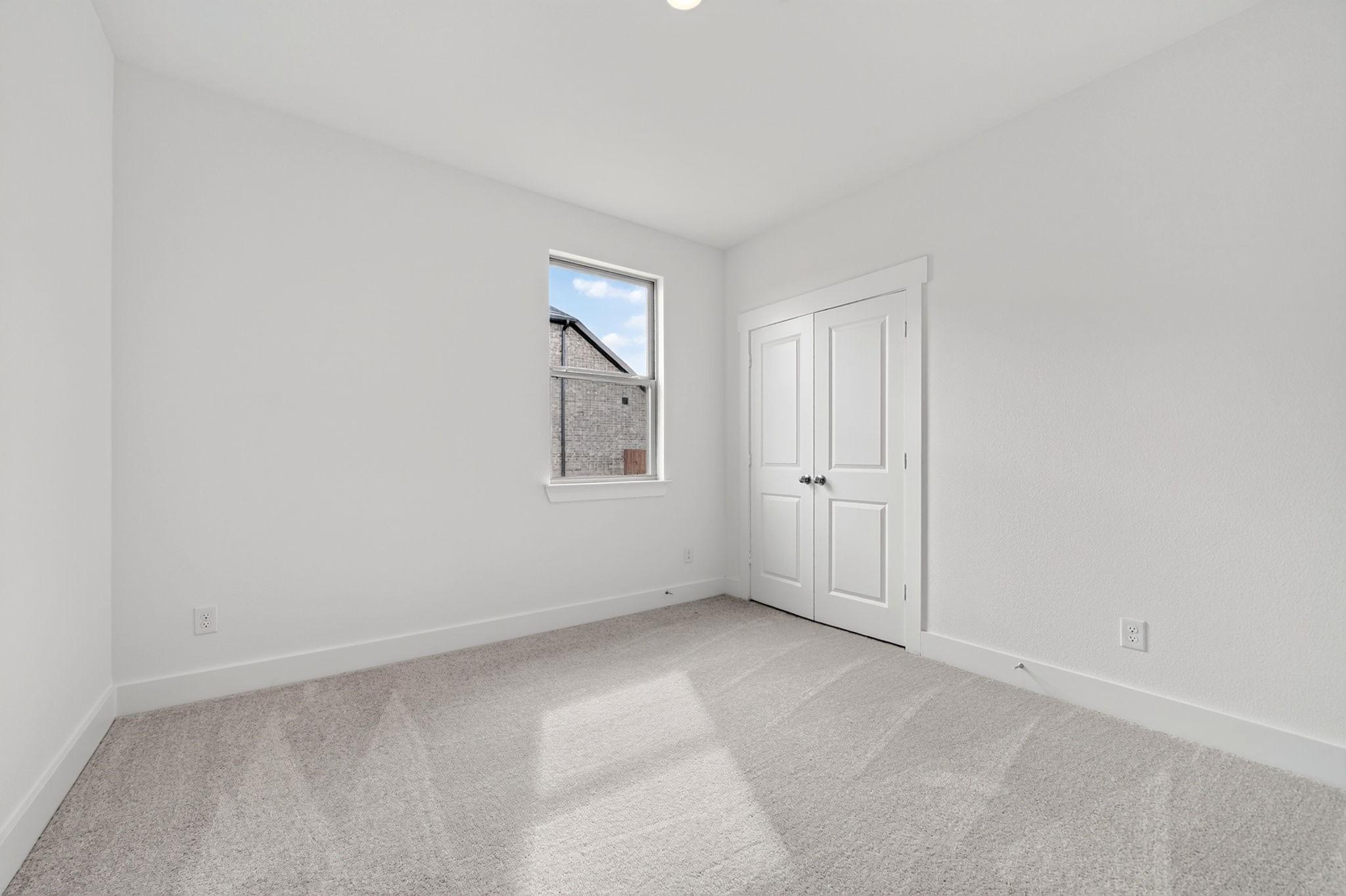 Bright white bedroom with plush carpet, double-door closet, and window in Davidson Homes The Holly F, Meadow Ridge Estates, Josephine, TX
