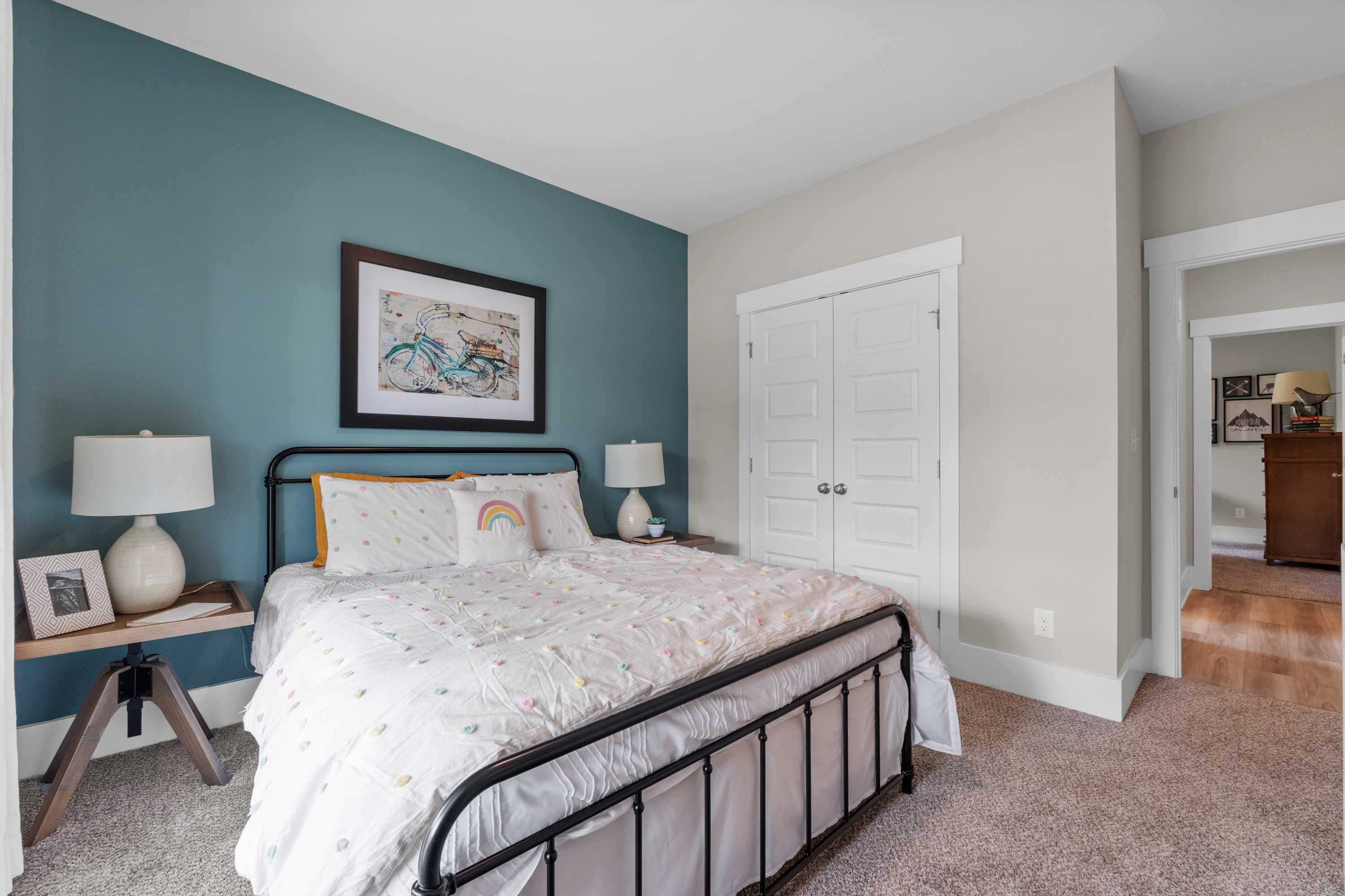 Cozy bedroom interior at The Highlands in Arab Alabama with teal accent wall, black metal bed frame, white bedding, yellow pillows, bedside lamps