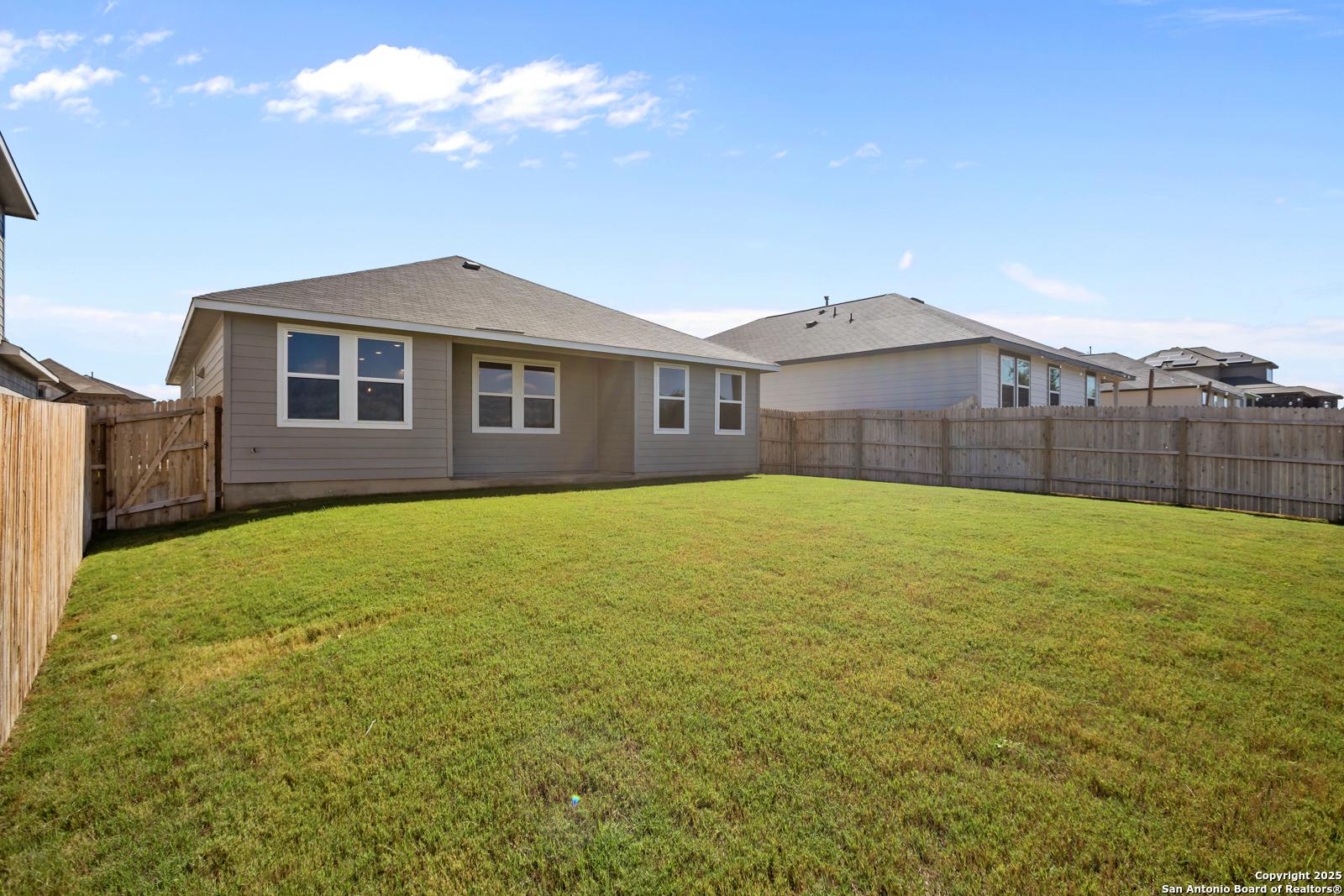 Expansive green lawn and wooden privacy fence in backyard of beige single-story home, Davidson Homes The Asheville H, Horizon Pointe, Converse, Texas