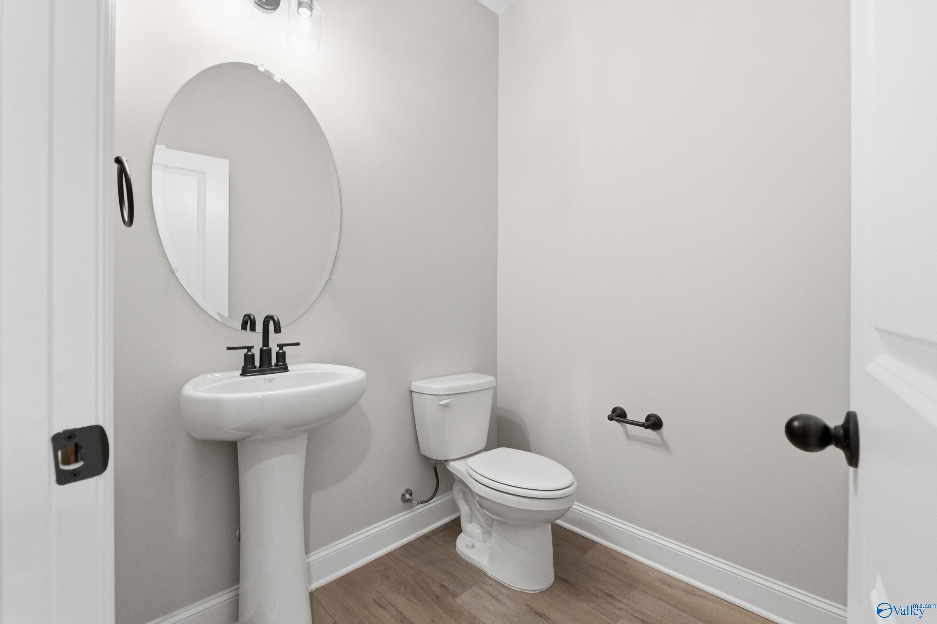 Modern powder room featuring pedestal sink, round mirror, and toilet in The Finleigh by Davidson Homes, Meridianville, Alabama