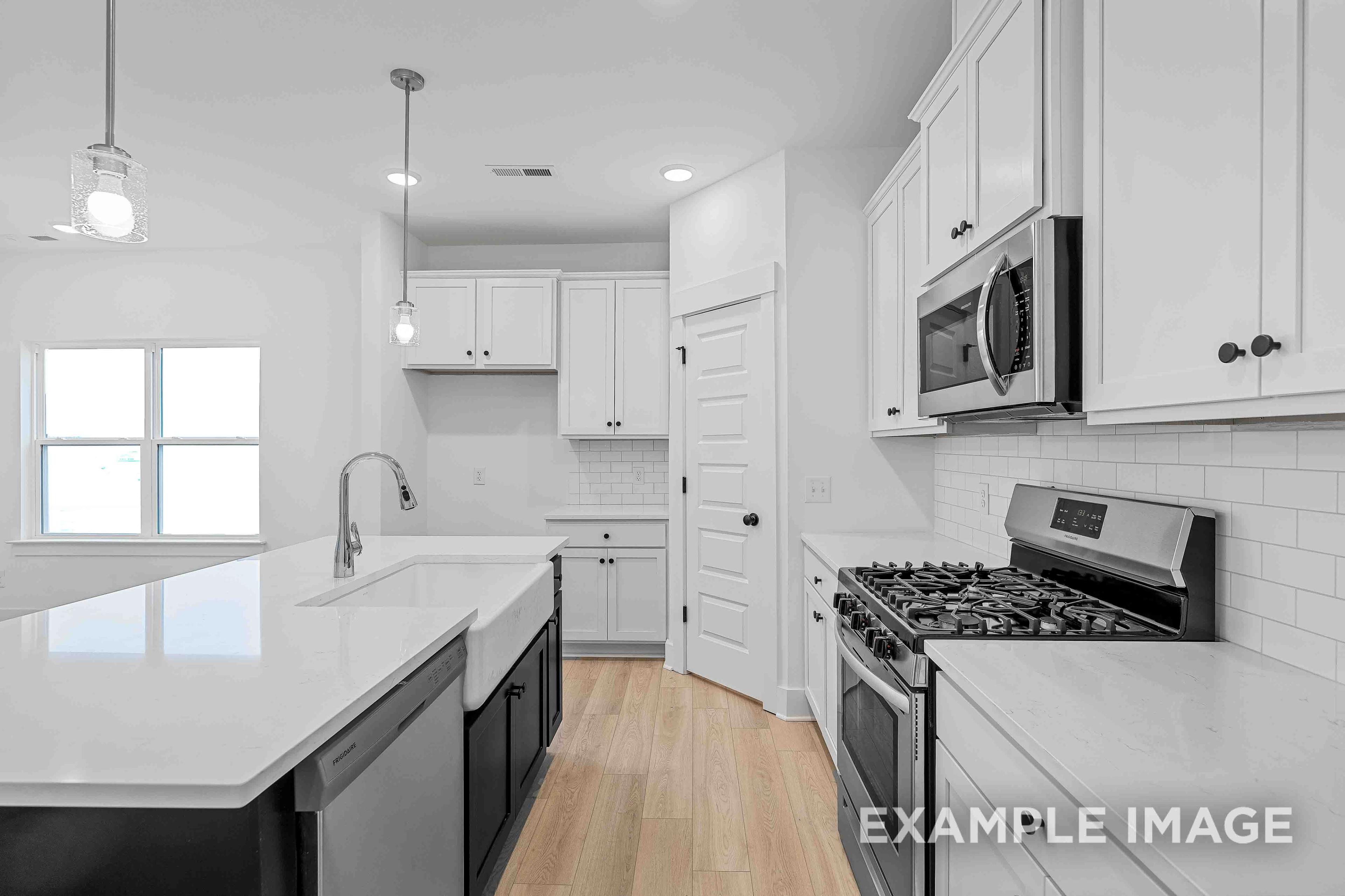Spacious modern kitchen in The Charleston featuring white shaker cabinets, large quartz island with farmhouse sink, gas range, and subway tile backsplash