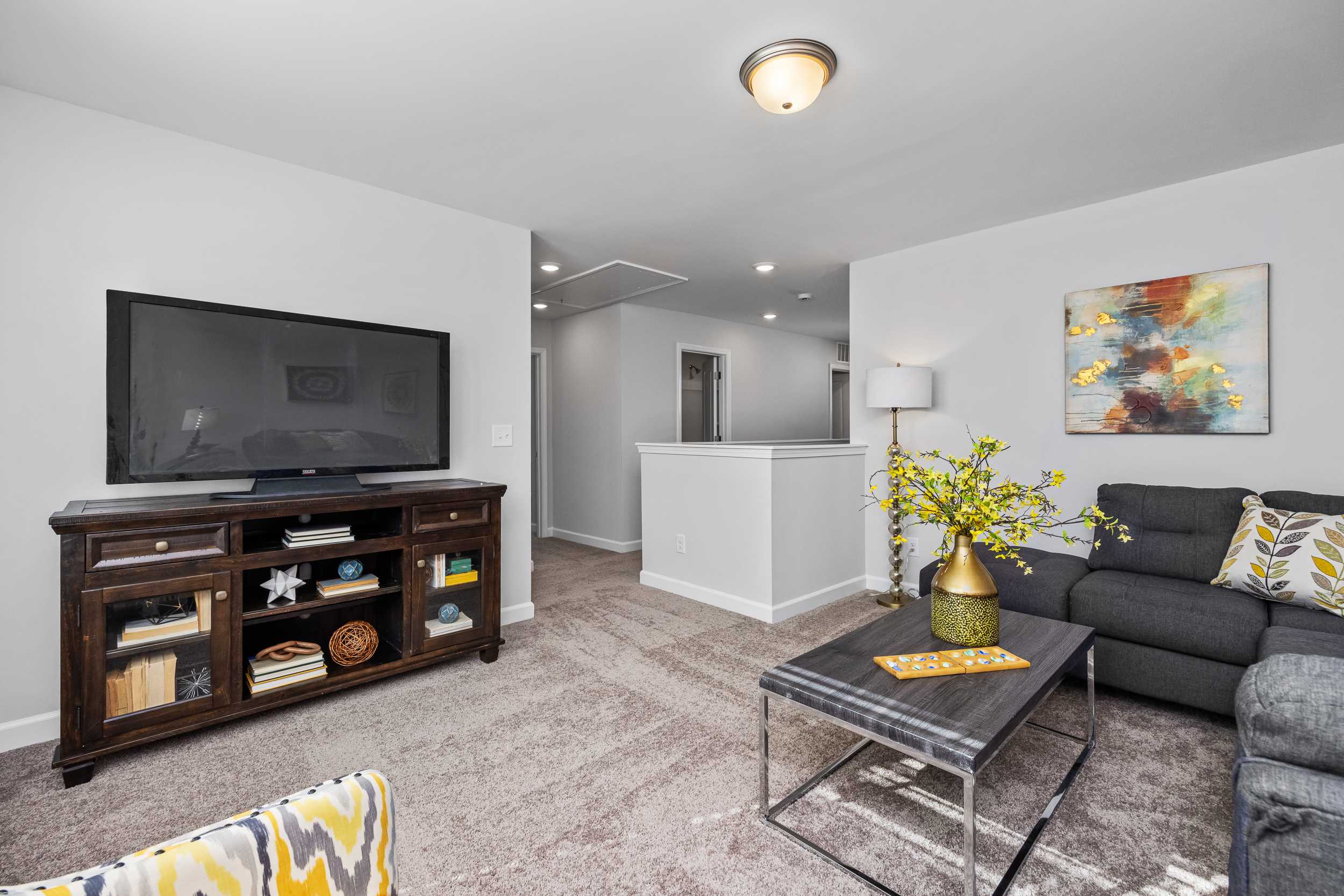 Cozy living room with wooden entertainment center, gray sofa, yellow flowers, abstract art and loft overlook at Woodland Crossing in Zebulon NC