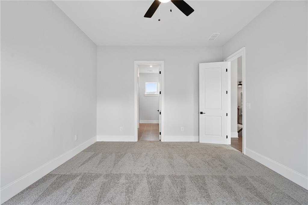 Spacious empty bedroom with ceiling fan, gray carpet, and open door to bath in Davidson Homes Seaside B, Woodstock GA