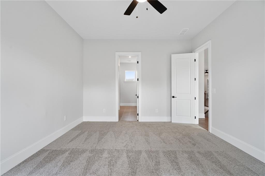 Spacious empty bedroom with ceiling fan, gray carpet, and open door to bath in Davidson Homes Seaside B, Woodstock GA