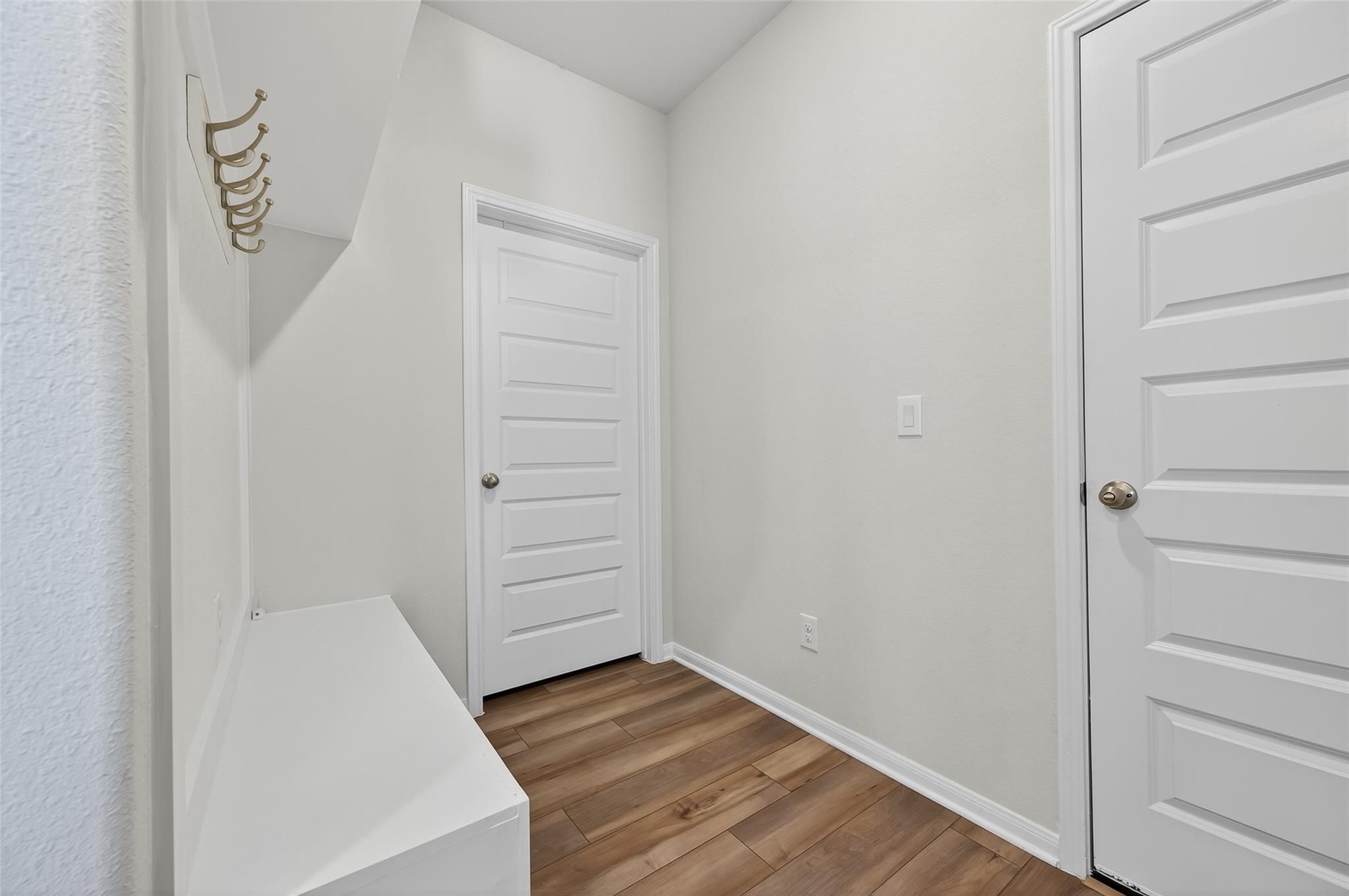 Bright mudroom with white bench, gold coat hooks, paneled doors in Davidson Homes The Brazos E, Magnolia, Texas