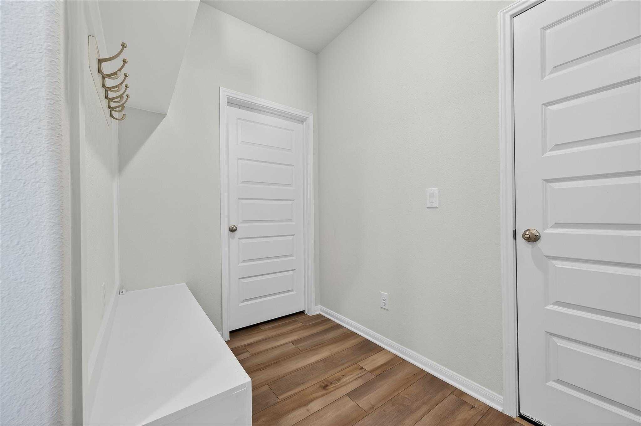 Bright mudroom with white bench, gold coat hooks, paneled doors in Davidson Homes The Brazos E, Magnolia, Texas