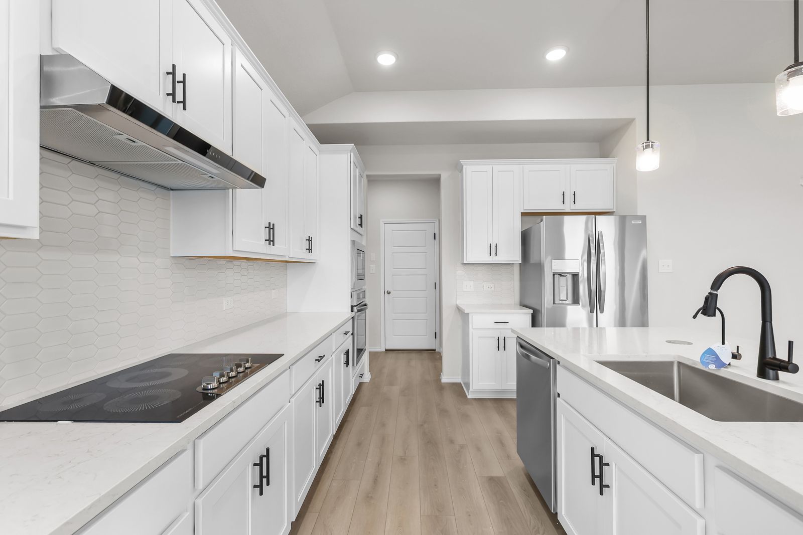 Modern white gourmet kitchen in The Sequoia C featuring quartz countertops, stainless steel appliances, and a large island.