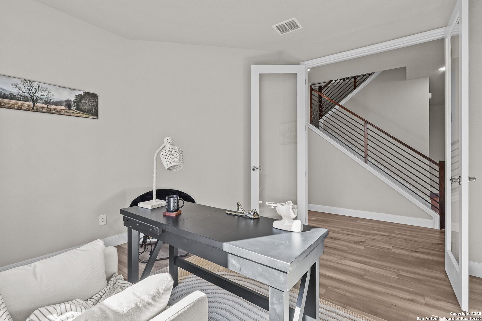 Cozy home office with wooden desk, white armchair, French doors to metal-railed staircase in Davidson Homes Jennings G, Castroville TX