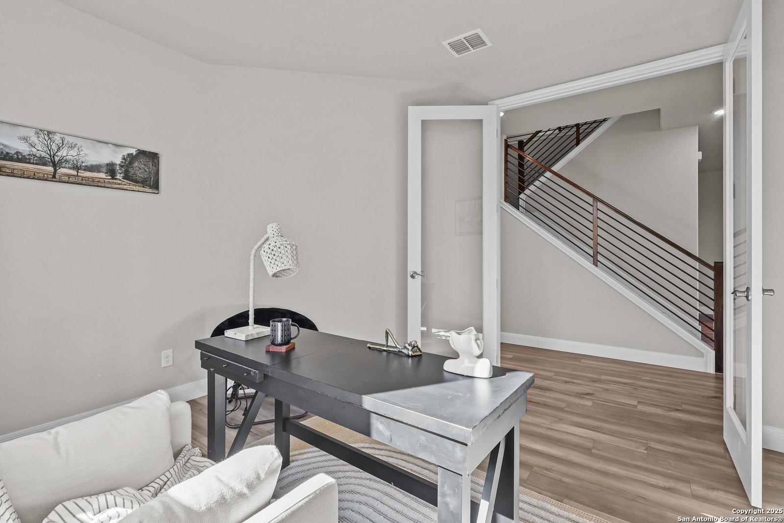 Cozy home office with wooden desk, white armchair, French doors to metal-railed staircase in Davidson Homes Jennings G, Castroville TX