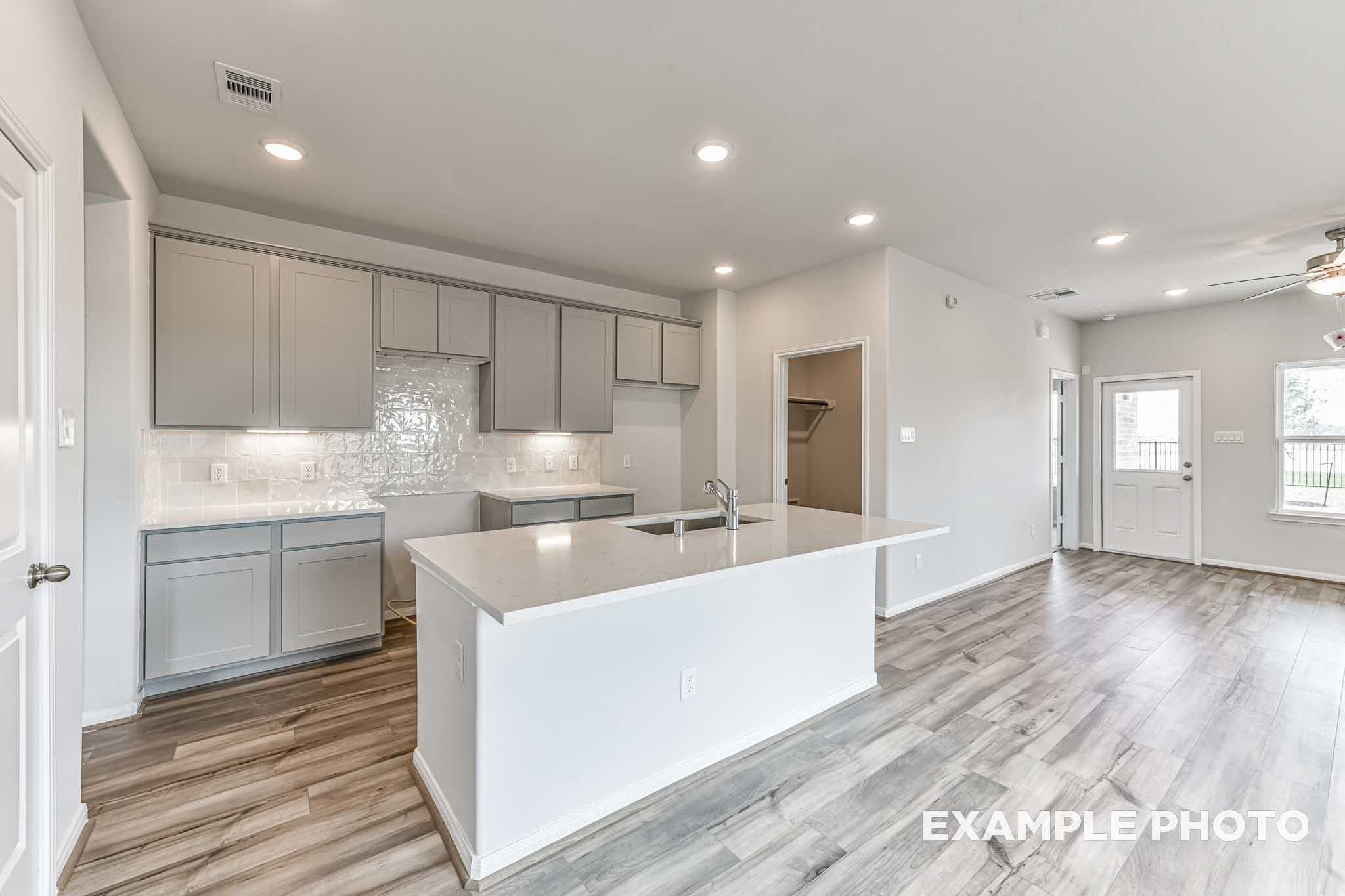 Modern kitchen in The Costa C featuring white quartz island, gray shaker cabinets, subway tile backsplash, open to living area