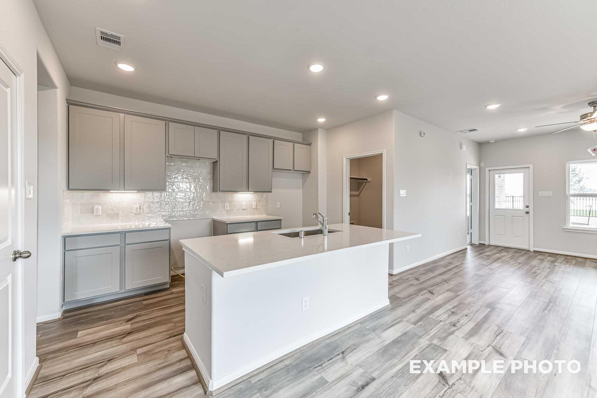 Spacious modern kitchen in The Costa A home with large white quartz island, gray shaker cabinets, subway tile backsplash, and open hardwood living area