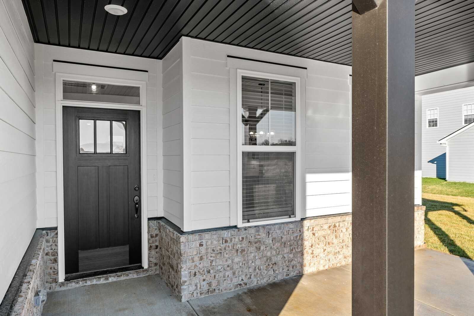 Inviting front porch with black paneled door, white siding, and stone accents on Davidson Homes The Willow B in Gallatin, Tennessee