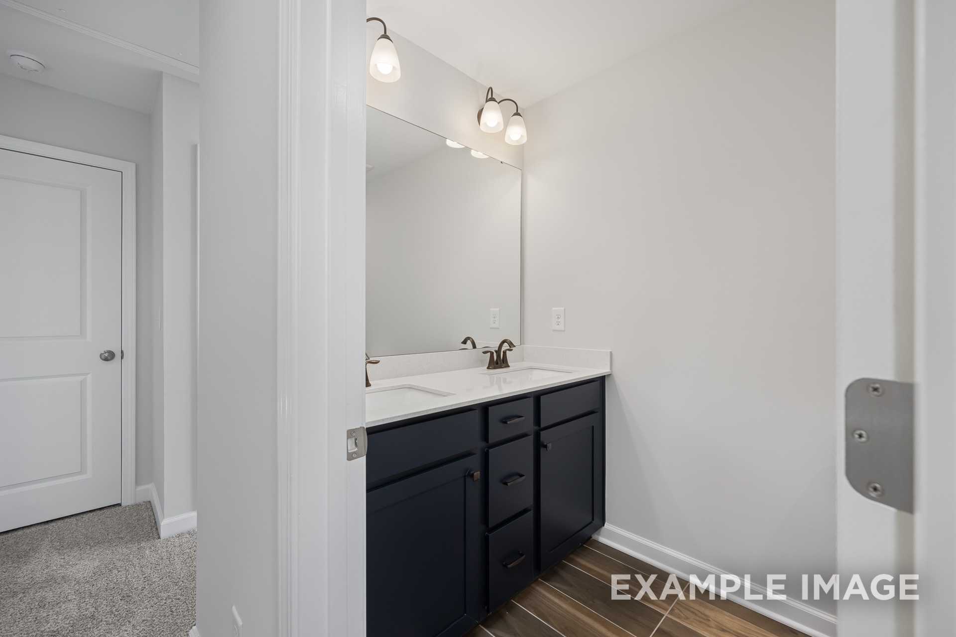 Modern master bathroom in The Grace C featuring double vanity with navy cabinets and lighted mirror