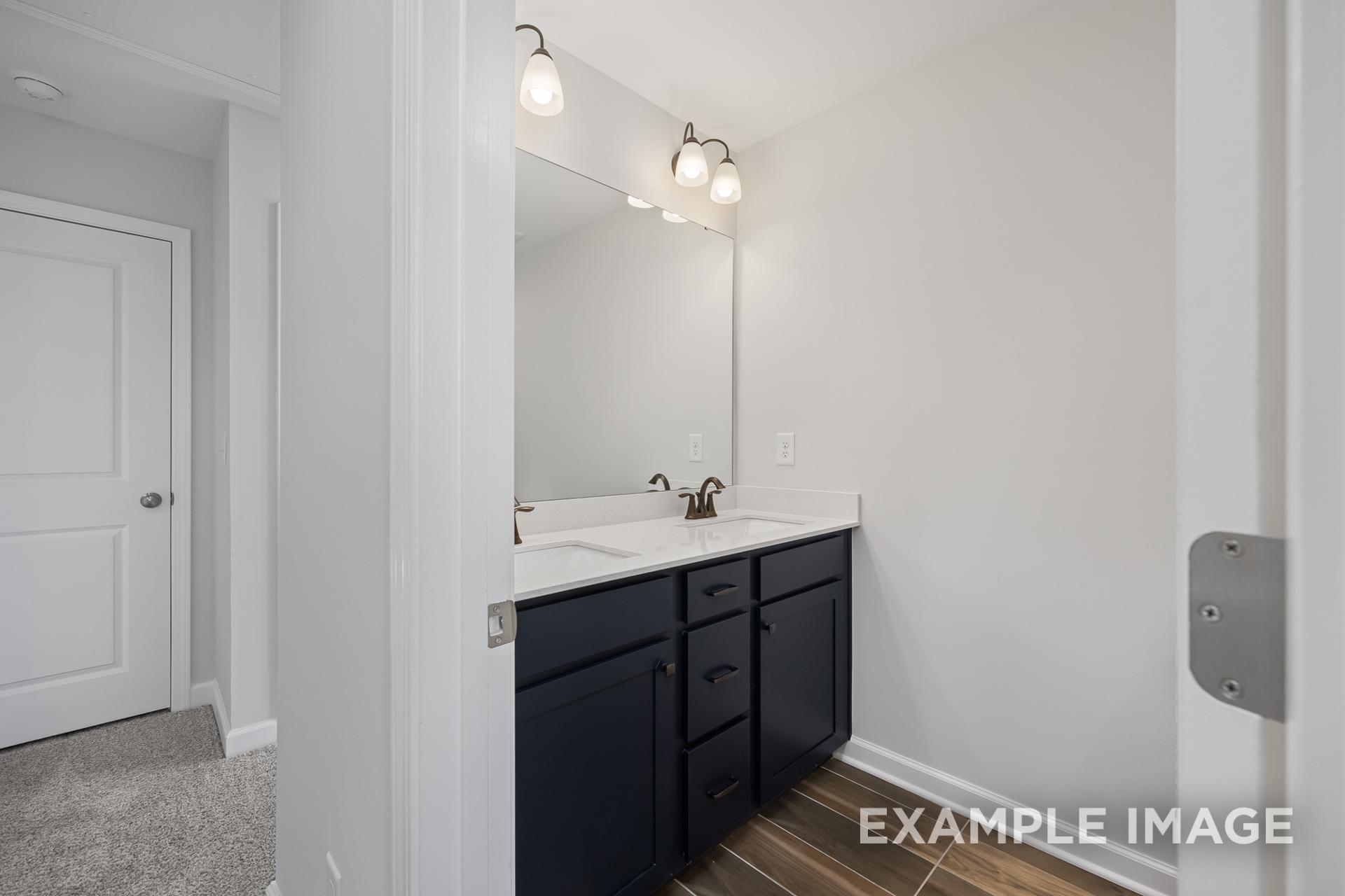 Modern master bathroom in The Grace C featuring double vanity with navy cabinets and lighted mirror