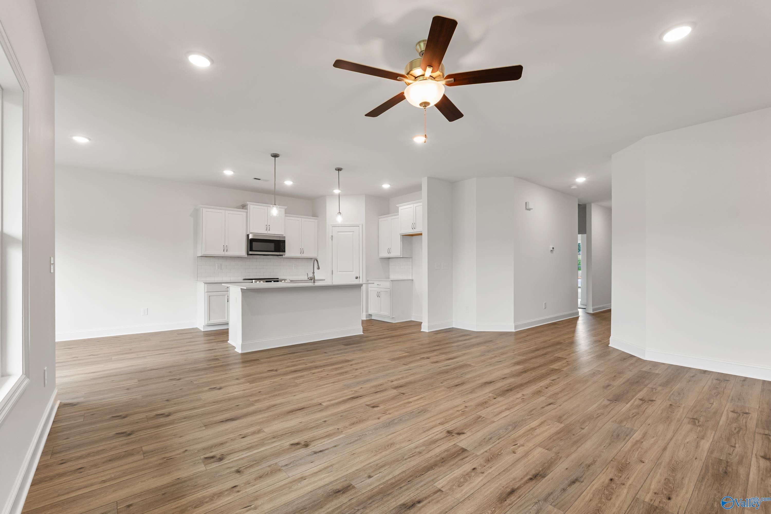 Open-concept kitchen and living area with white cabinetry, large island, ceiling fan, and hardwood floors in Davidson Homes The Asheville C, New Market, Alabama