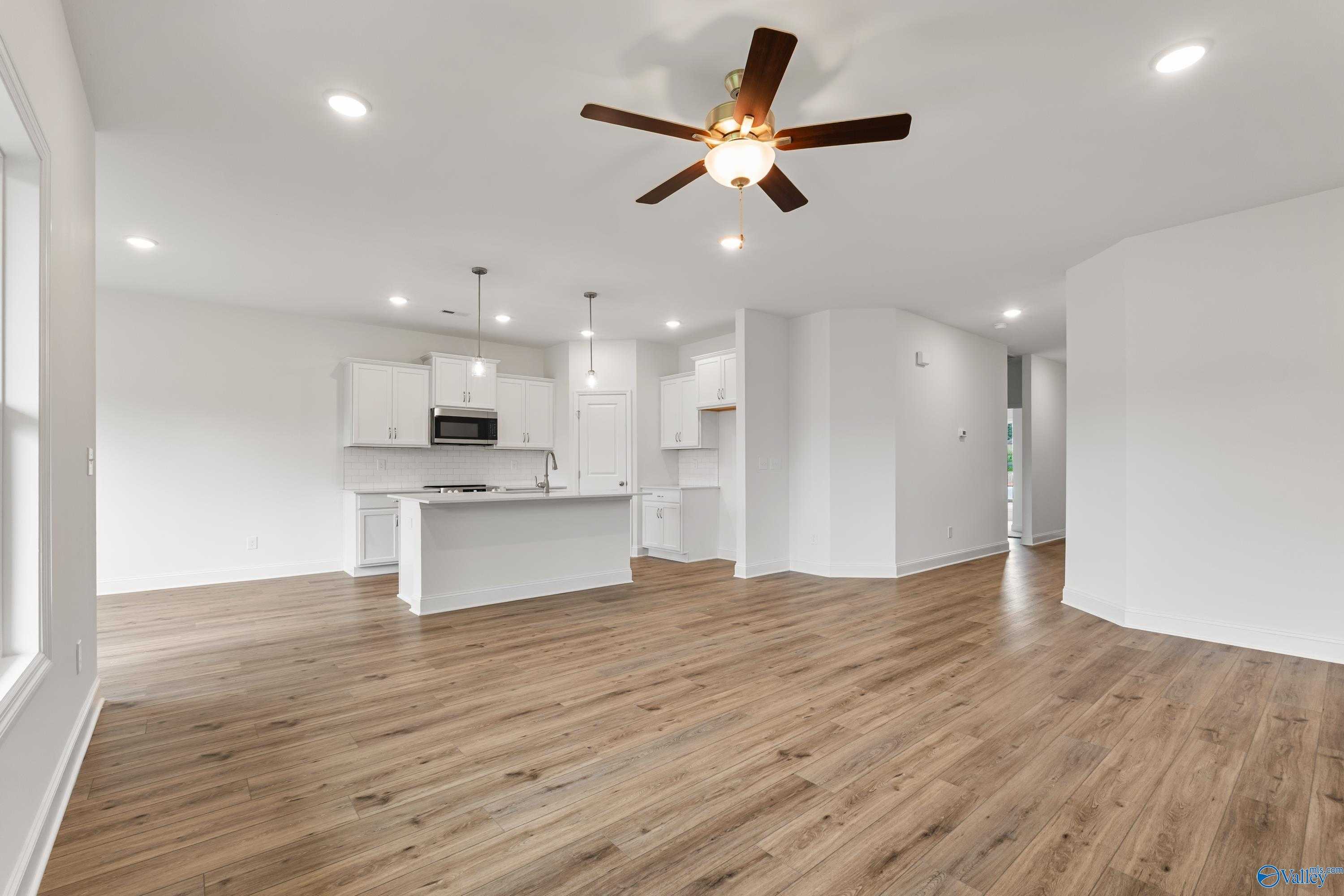 Open-concept kitchen and living area with white cabinetry, large island, ceiling fan, and hardwood floors in Davidson Homes The Asheville C, New Market, Alabama