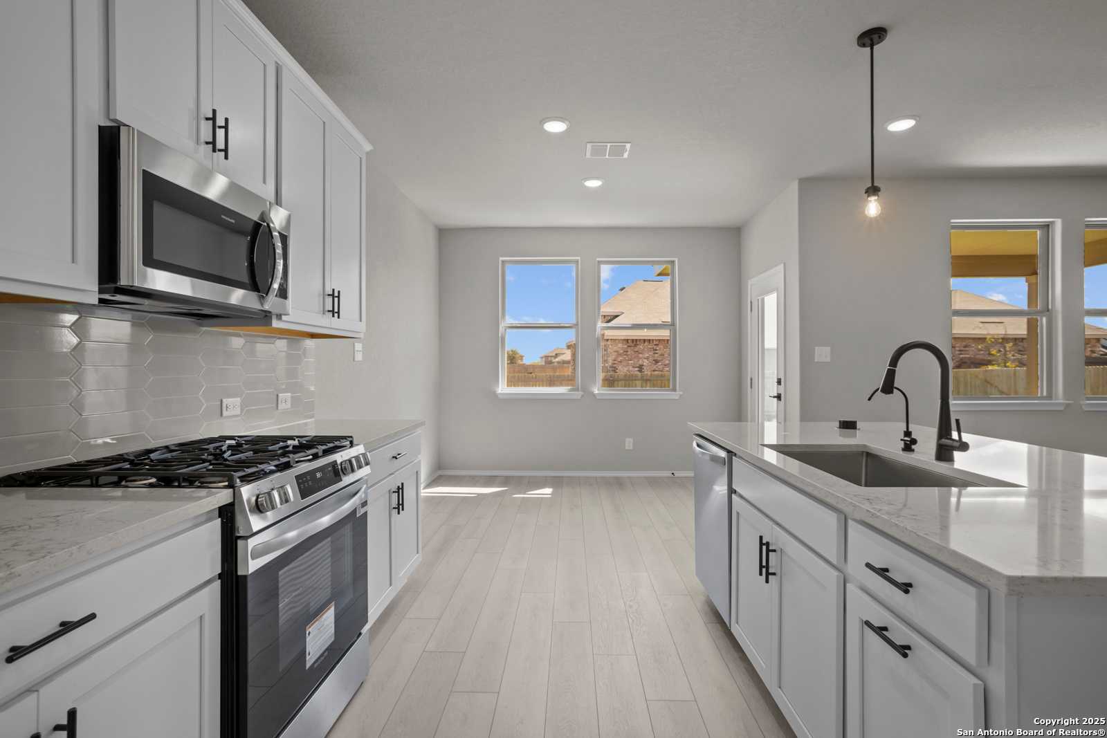 Modern open-concept kitchen with white cabinets, stainless steel appliances, quartz island, and large windows in Davidson Homes Asheville E, Converse TX