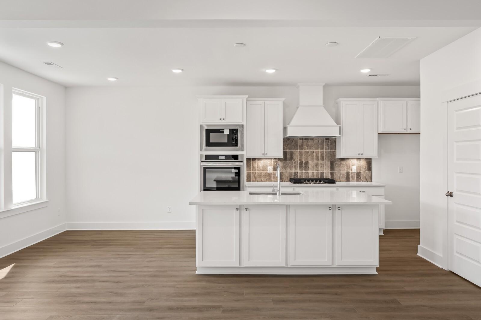Modern white kitchen with large island, stainless double ovens, and subway tile backsplash in Davidson Homes The Willow D, Mt. Juliet