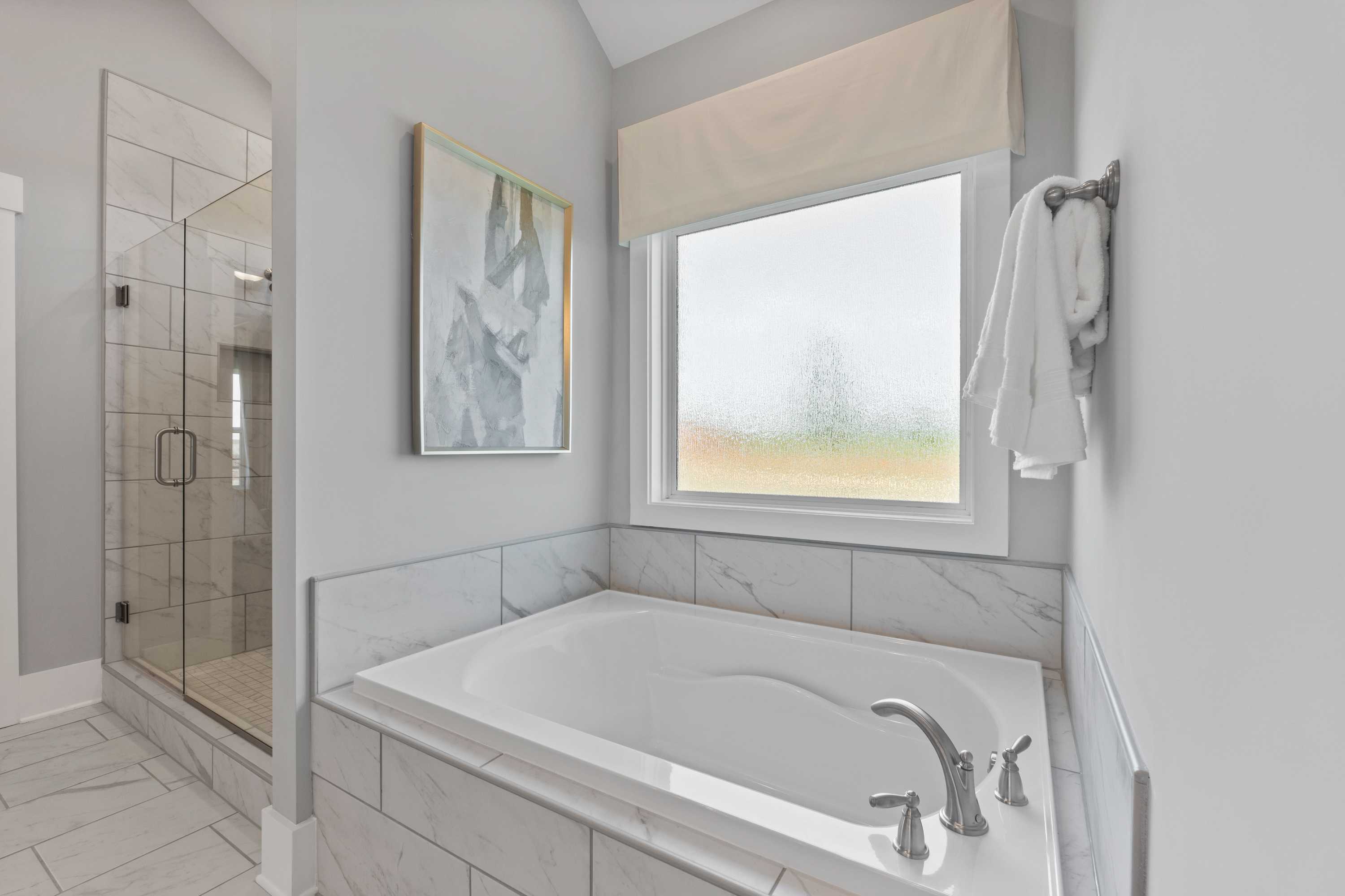 Luxurious primary bathroom in Creekside at Harvest, Alabama featuring freestanding tub, glass shower, and abstract art