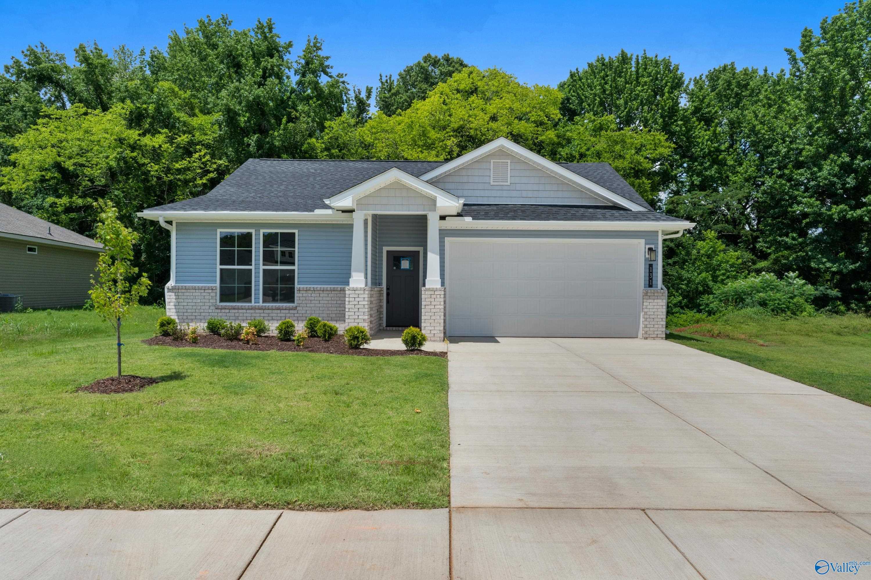 Light blue single-story 3-bedroom home with 2-car garage, brick accents, and lush green lawn in Forest Glen, Hazel Green, Alabama