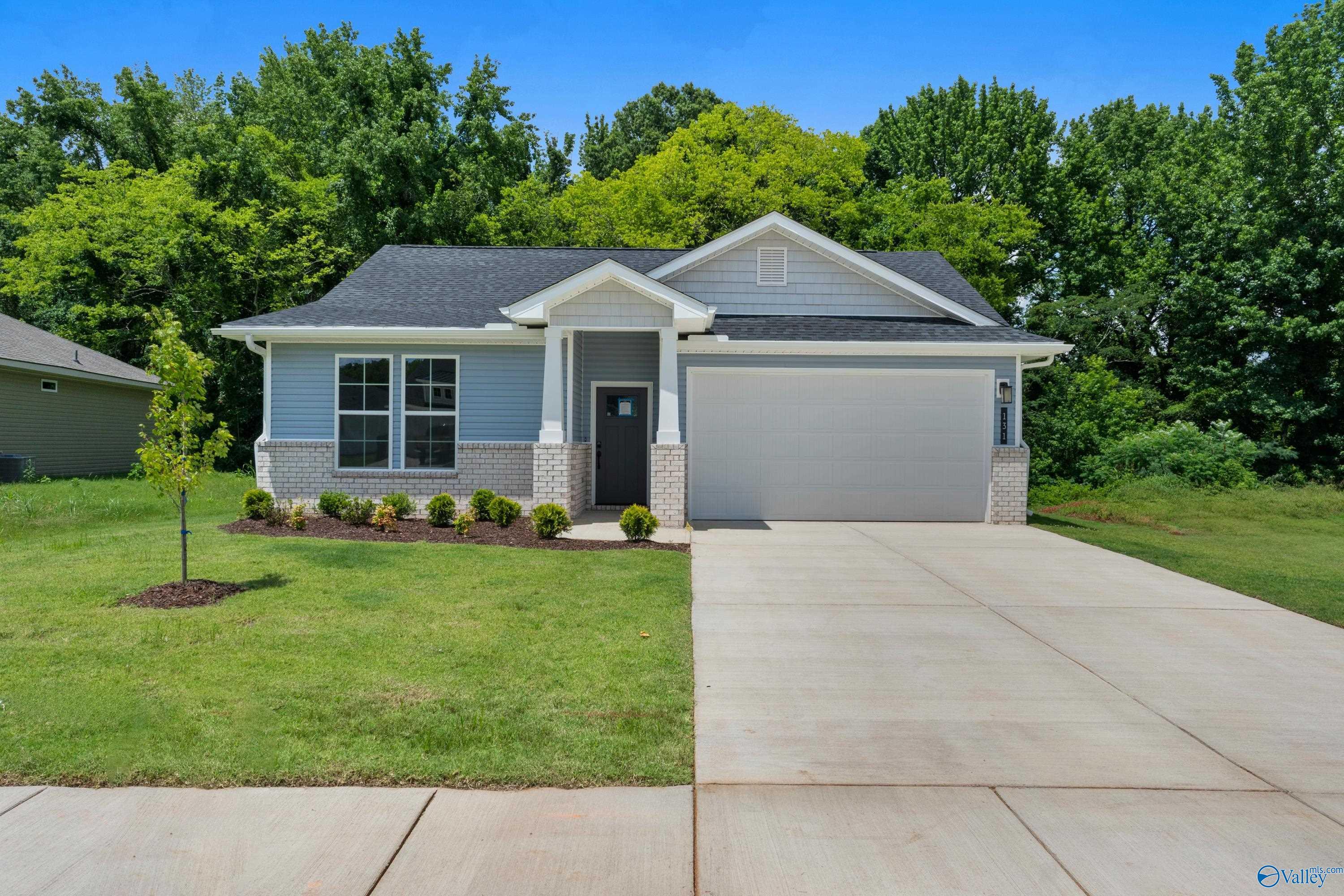 Light blue single-story 3-bedroom home with 2-car garage, brick accents, and lush green lawn in Forest Glen, Hazel Green, Alabama