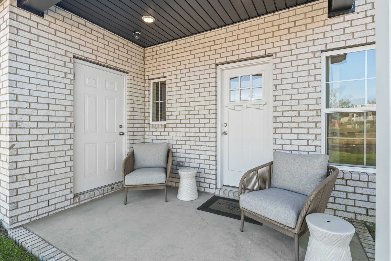 Inviting front porch with white brick exterior, double doors, and gray cushioned chairs in Davidson Homes The Cumberland B, Gallatin, Tennessee